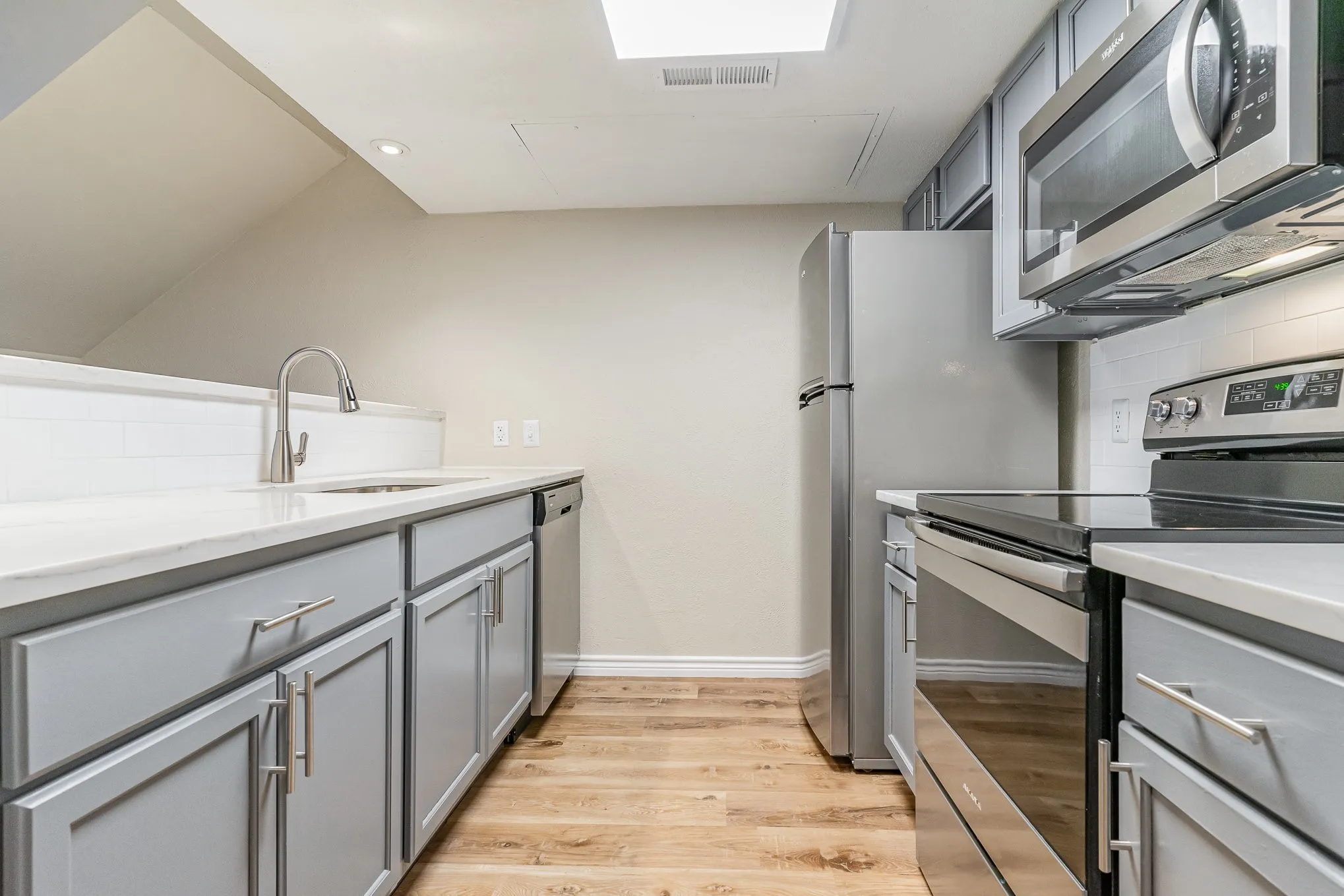 Kitchen with stainless steel appliances, visible vents, gray cabinets, a sink, and light wood-style flooring