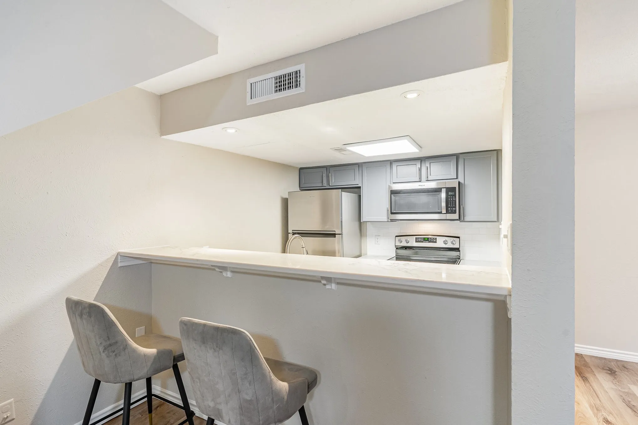 Kitchen with light wood-style floors, gray cabinets, a kitchen bar, appliances with stainless steel finishes, and visible vents