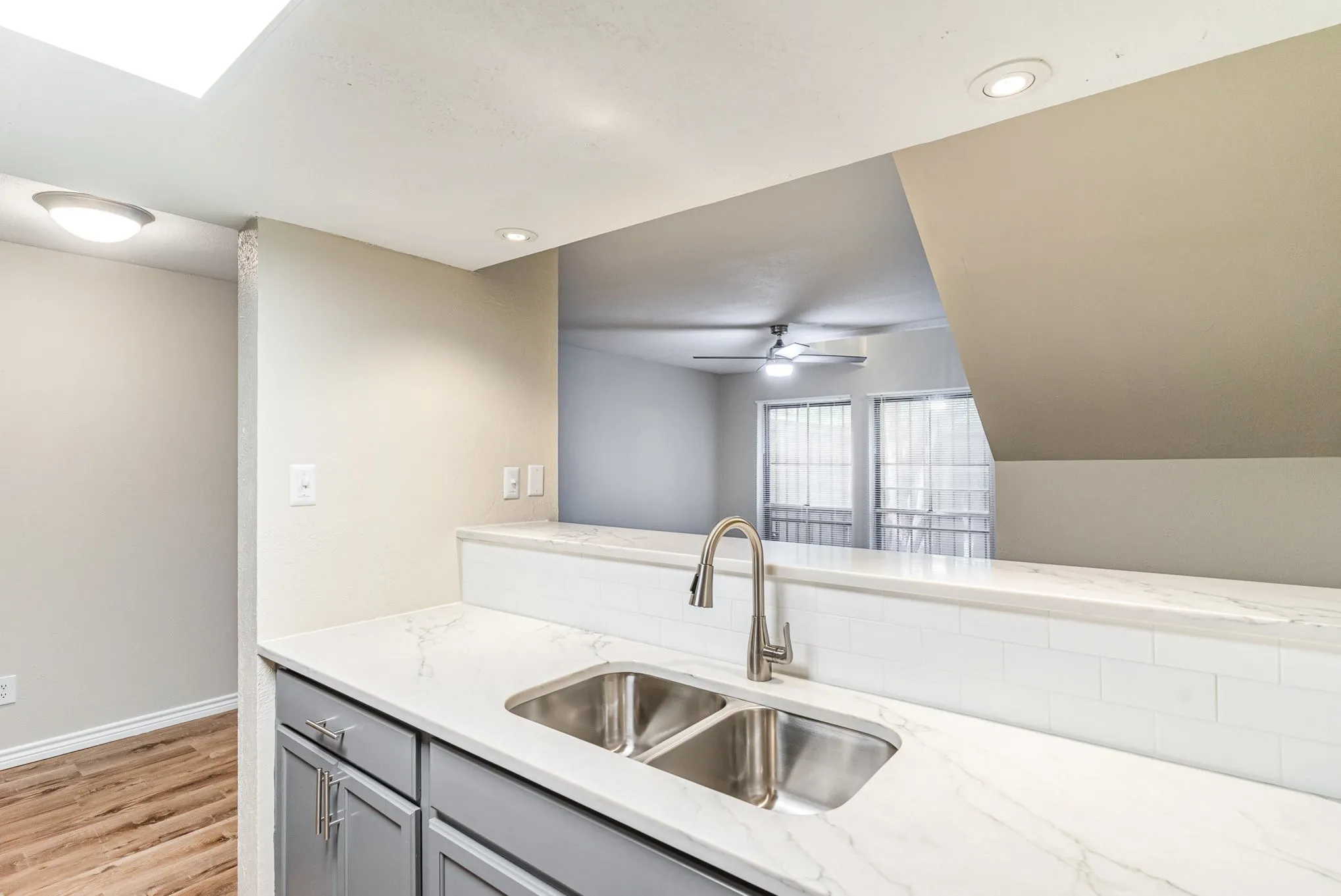 Kitchen with a ceiling fan, gray cabinets, a sink, light wood-style floors, and light stone countertops