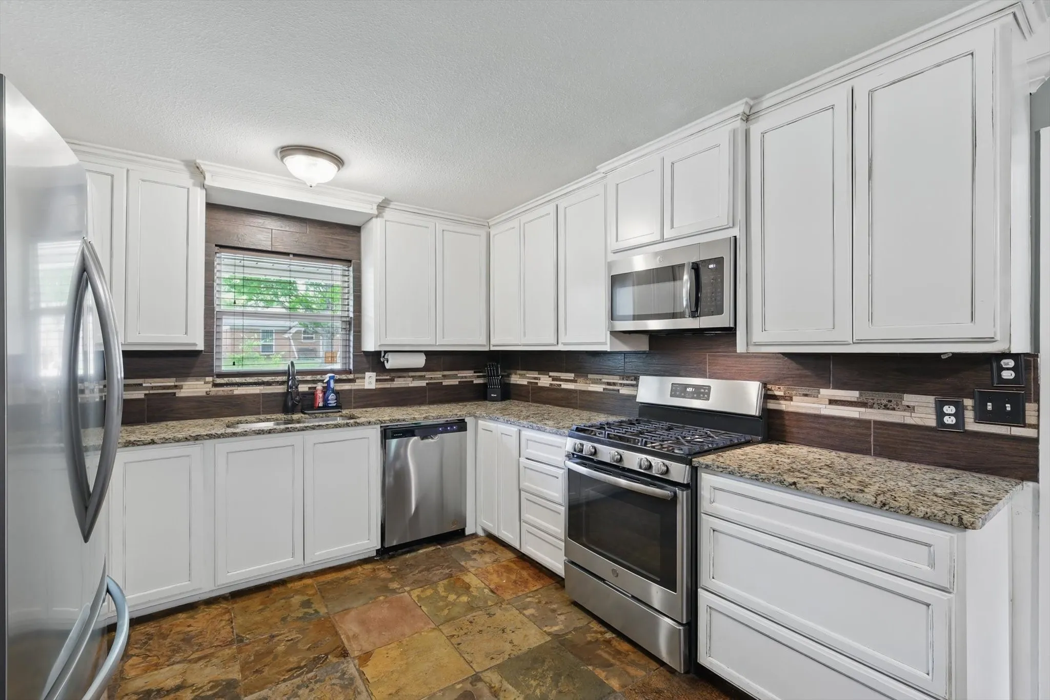 Kitchen with white cabinets, appliances with stainless steel finishes, a sink, and tasteful backsplash