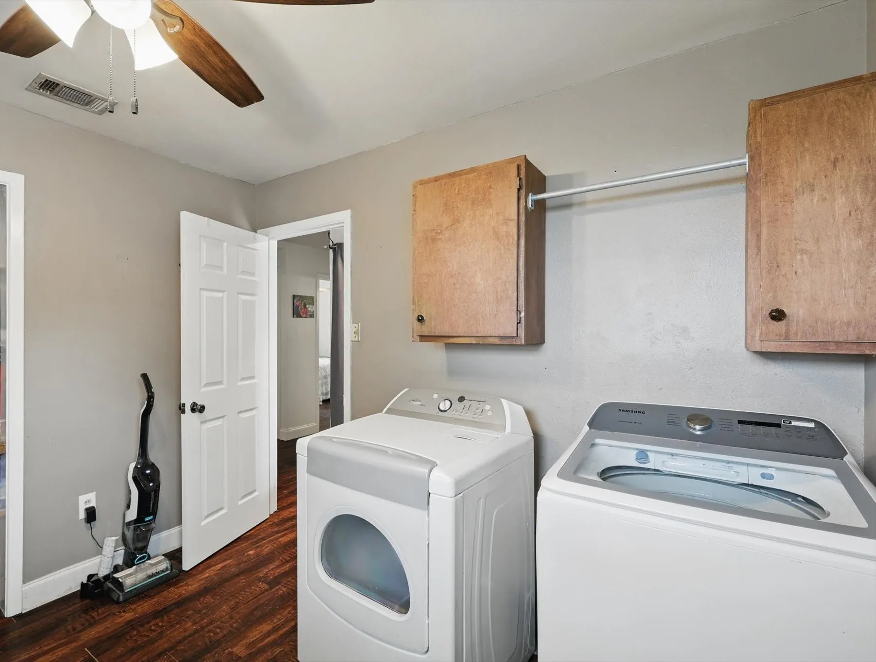 Washroom featuring visible vents, ceiling fan, dark wood-style floors, washer and clothes dryer, and cabinet space