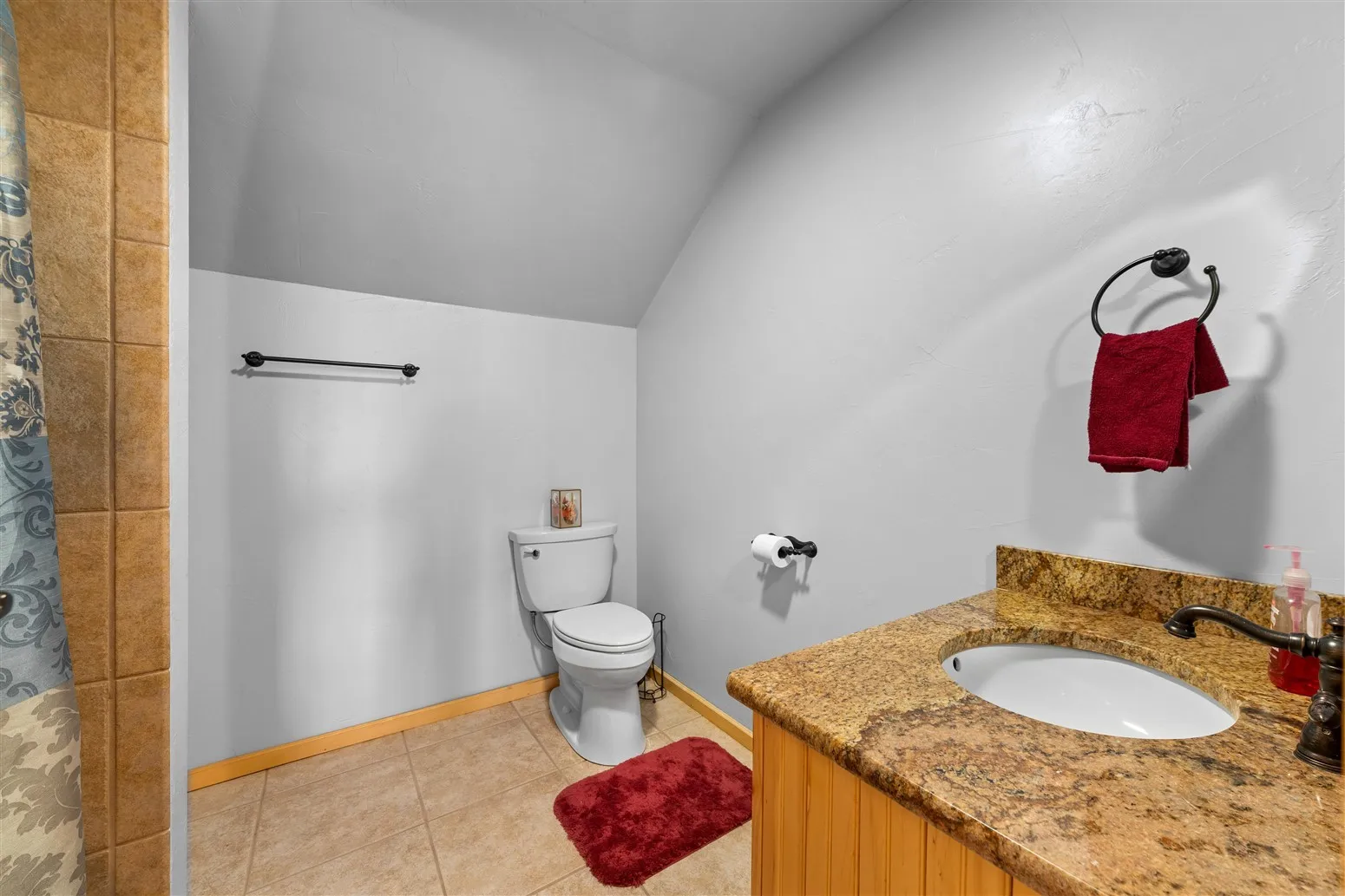 Bathroom with tile patterned floors, a sink, toilet, lofted ceiling, and curtained shower