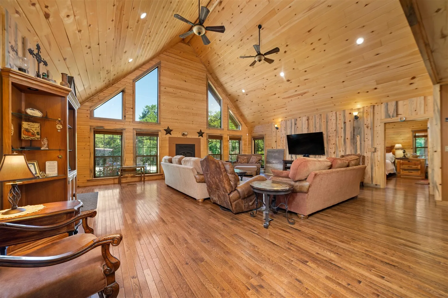Living room with light wood finished floors, wood walls, a fireplace, high vaulted ceiling, and ceiling fan
