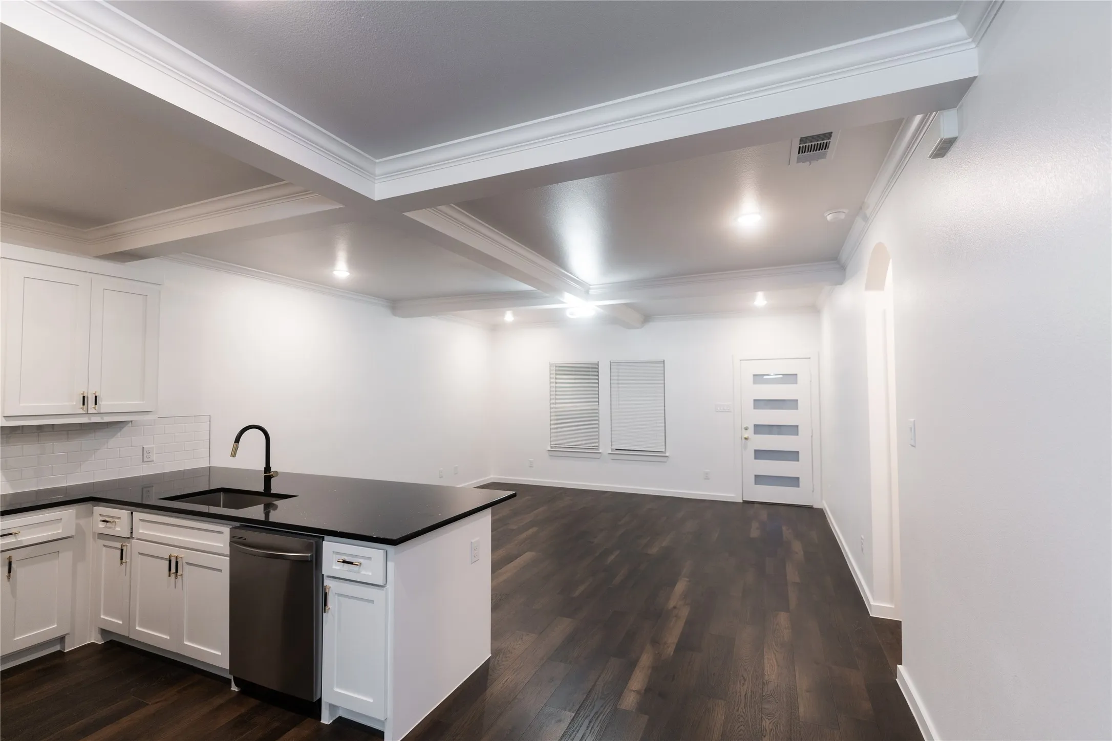 Kitchen with dark countertops, dishwasher, a sink, visible vents, and a peninsula