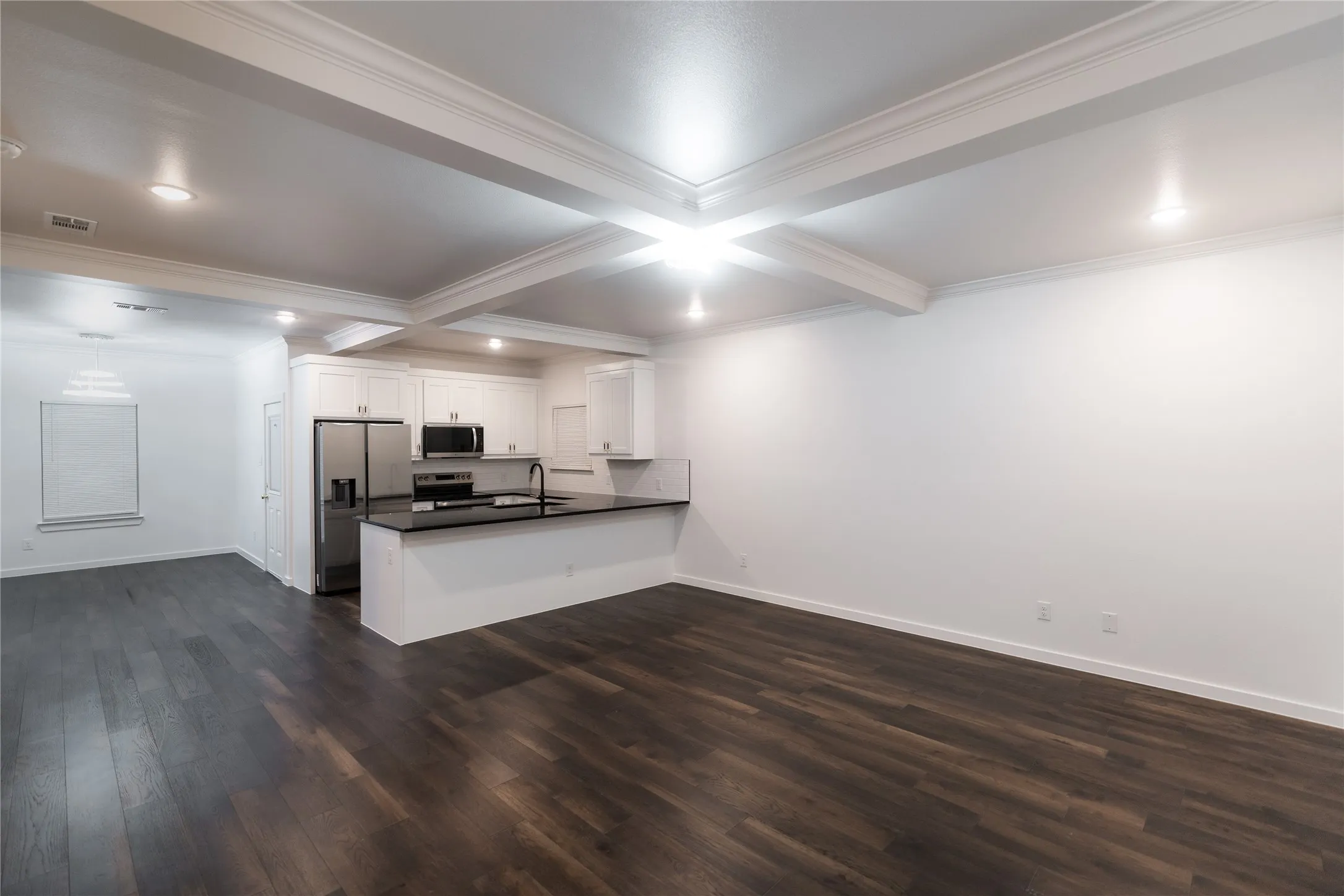 Kitchen featuring dark wood-style floors, crown molding, a peninsula, dark countertops, and appliances with stainless steel finishes