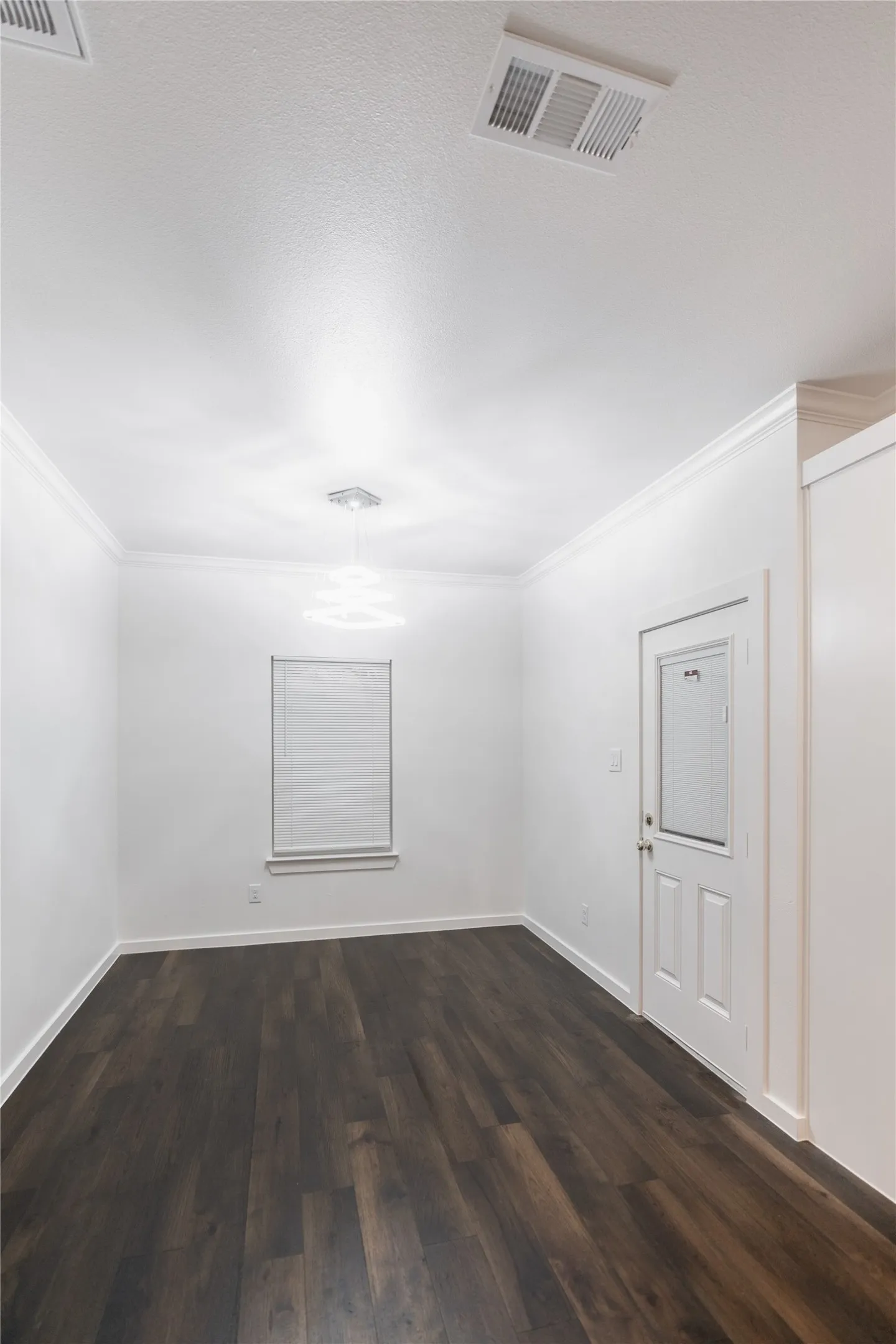 Spare room featuring dark wood-style floors, visible vents, crown molding, and baseboards