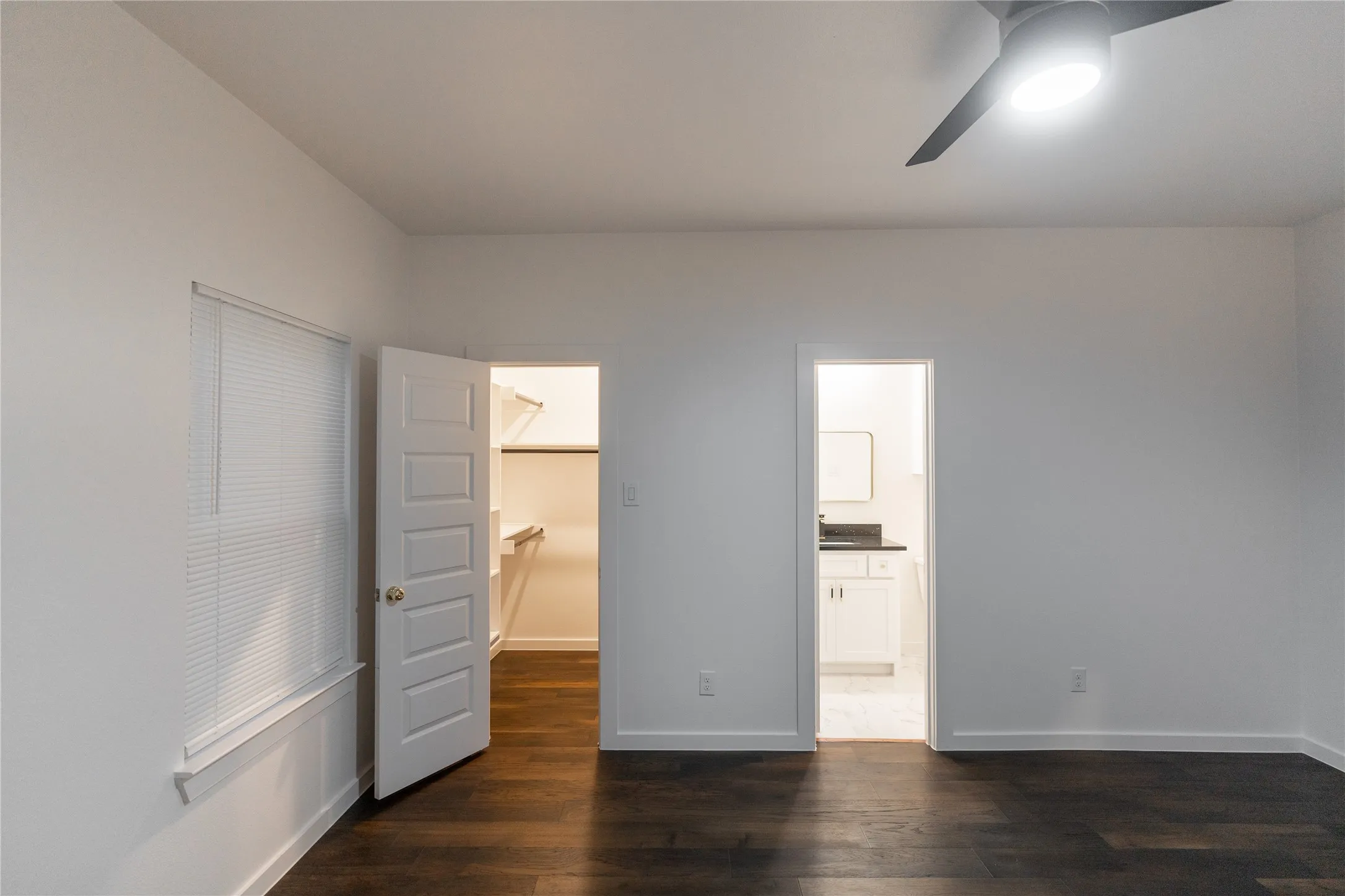 Unfurnished bedroom featuring ensuite bathroom, dark wood-style floors, a closet, baseboards, and a spacious closet