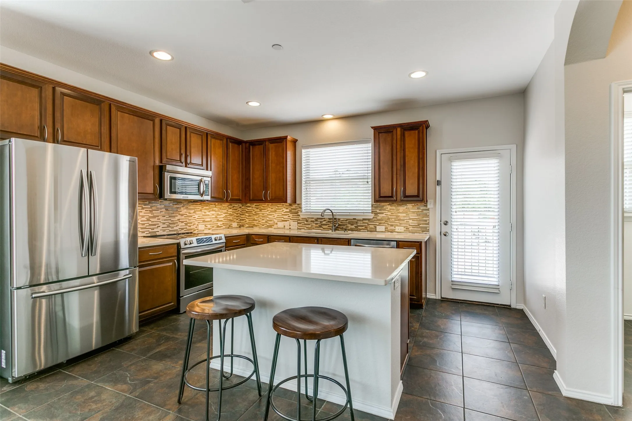 Featuring an island, appliances with stainless steel finishes, and tasteful backsplash, refrigerator included