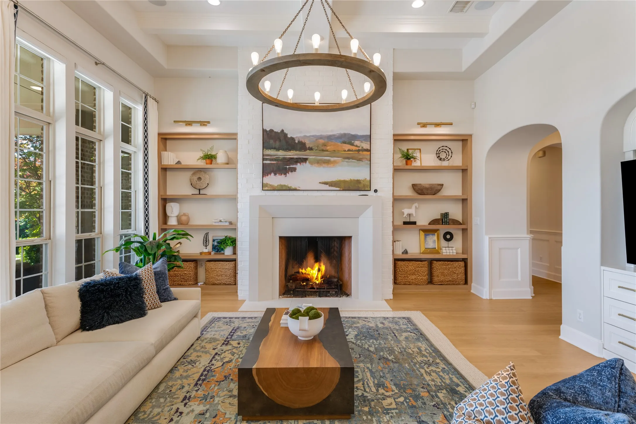A stunning example of luxury & comfort in the grand family room, the focal point of the fireplace is flanked by white oak built-ins & another tray ceiling featuring two contemporary chandeliers. AirPlay 2 speakers are tucked into ceilings throuhout the residence for the ability to flow music room to room.
