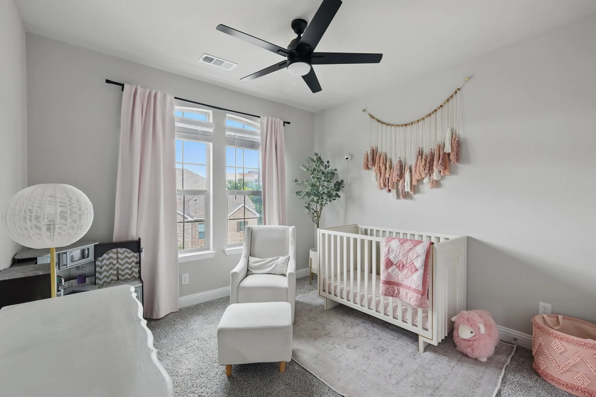 Carpeted bedroom with a ceiling fan, a nursery area, baseboards, and visible vents