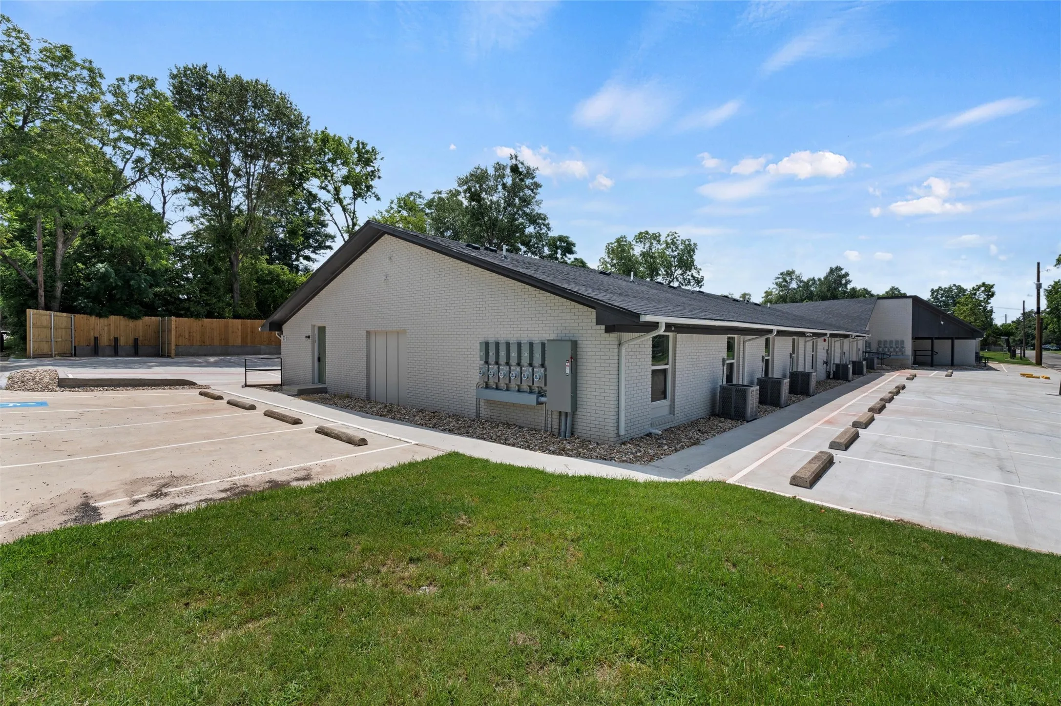 View of property exterior featuring uncovered parking, central AC, fence, brick siding, and a yard