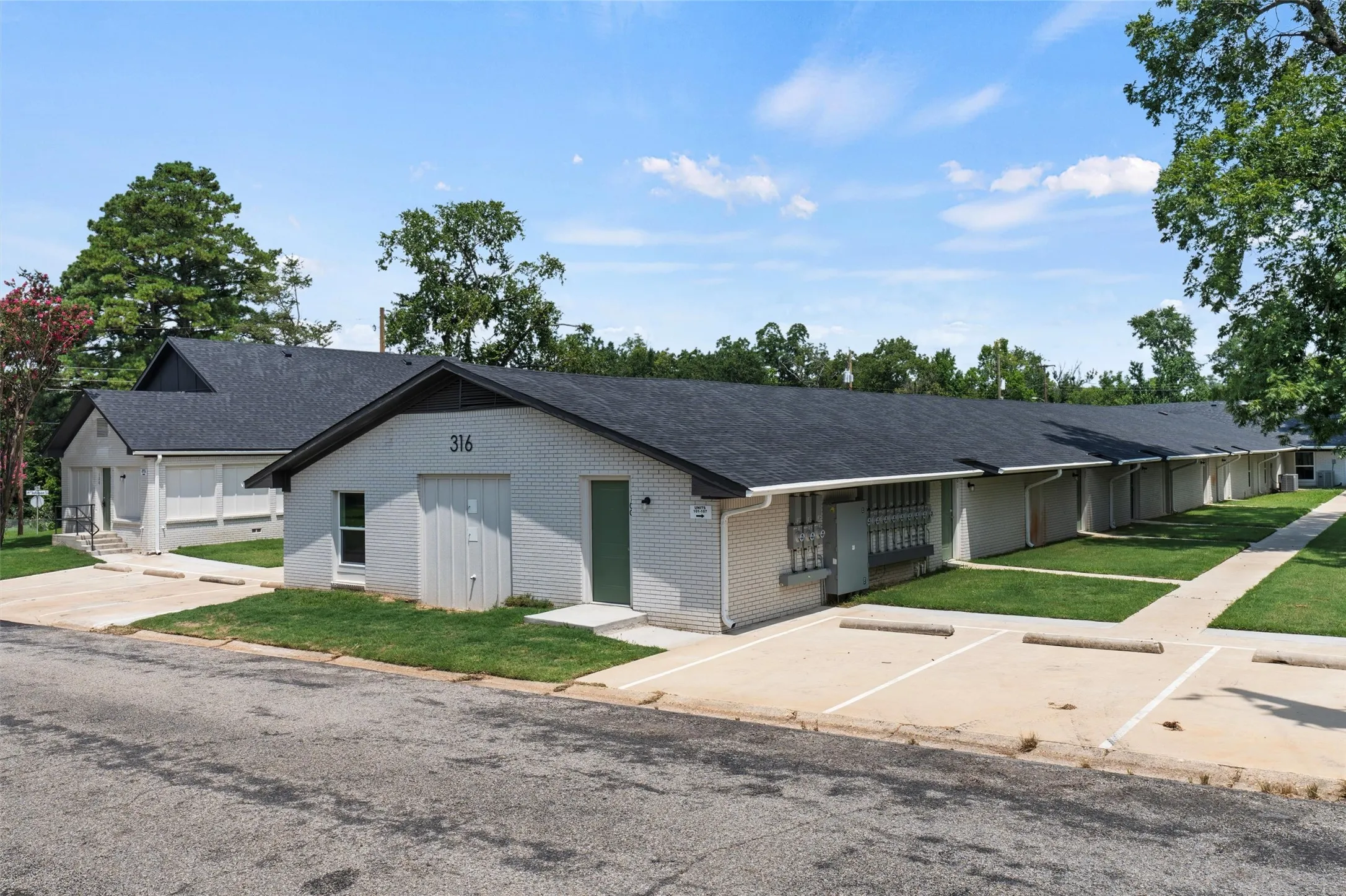 View of front of home featuring a shingled roof, a front lawn, uncovered parking, and brick siding
