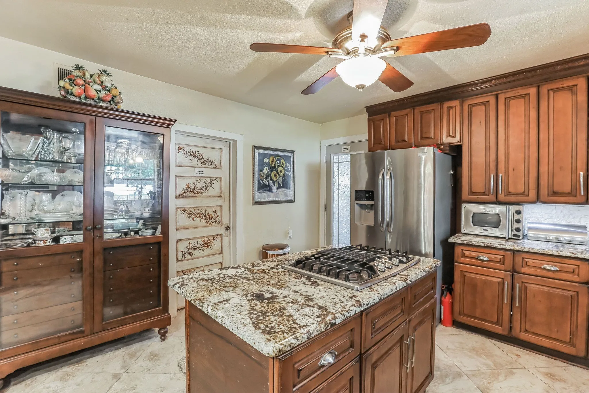 Kitchen with light stone counters, a kitchen island, brown cabinets, ceiling fan, and appliances with stainless steel finishes