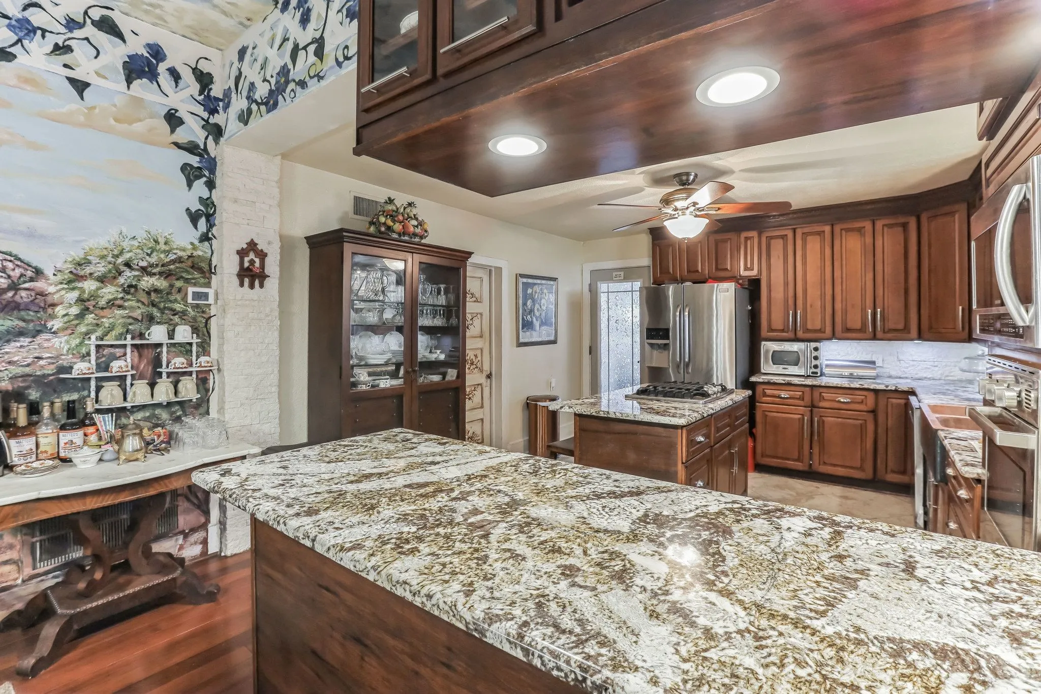 Kitchen with glass insert cabinets, a center island, light stone countertops, ceiling fan, and stainless steel appliances