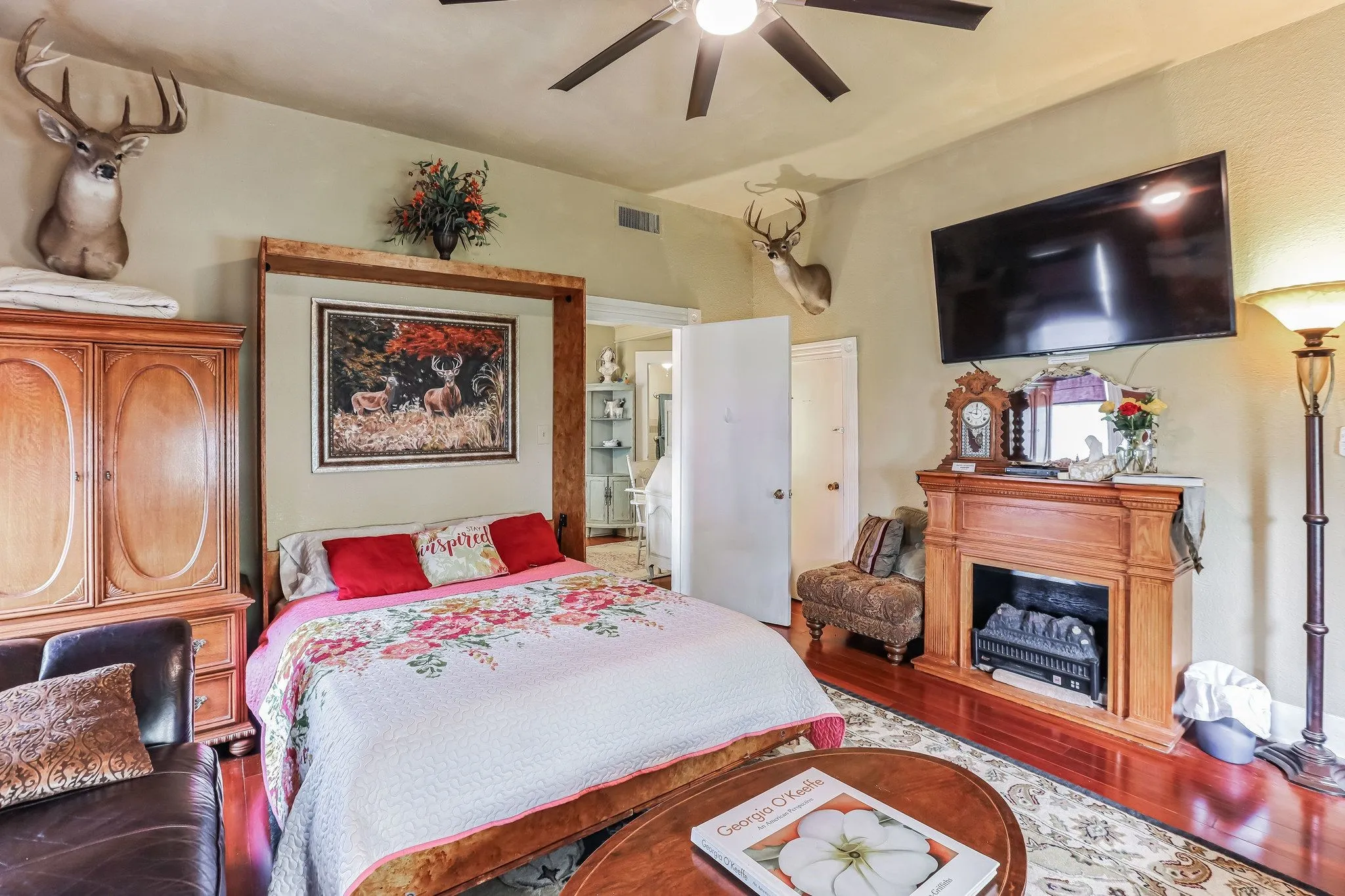 Bedroom with wood finished floors, ceiling fan, a fireplace, and visible vents