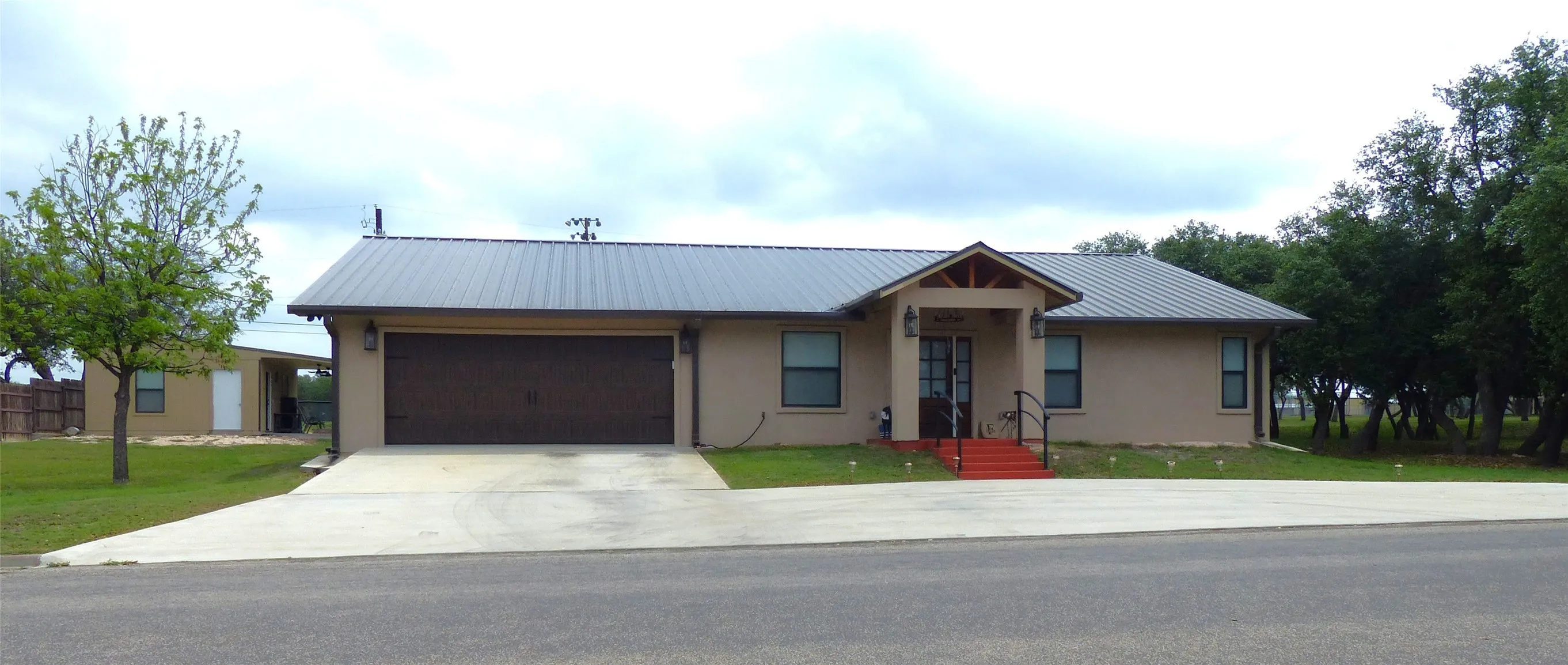 Ranch-style house featuring metal roof, a front yard, concrete driveway, an attached garage, and stucco siding