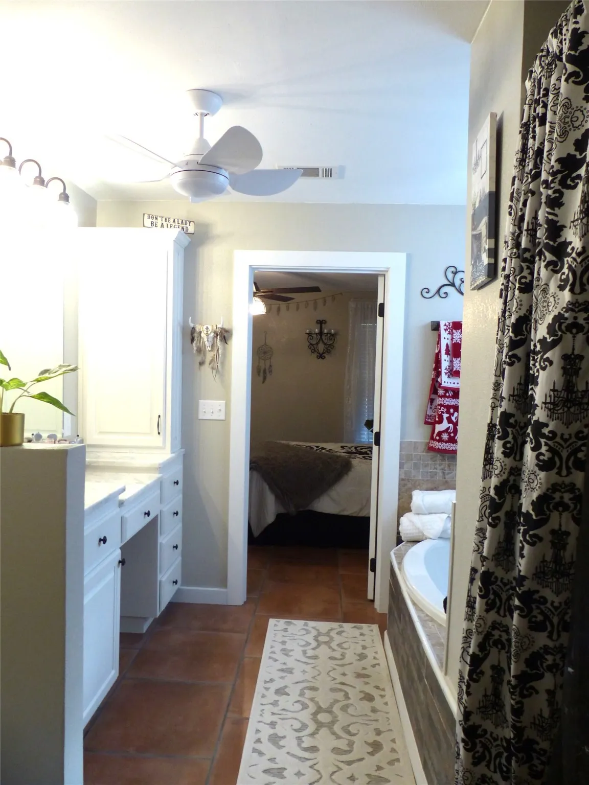 Ensuite bathroom featuring dark tile patterned floors, tiled tub, a ceiling fan, and vanity