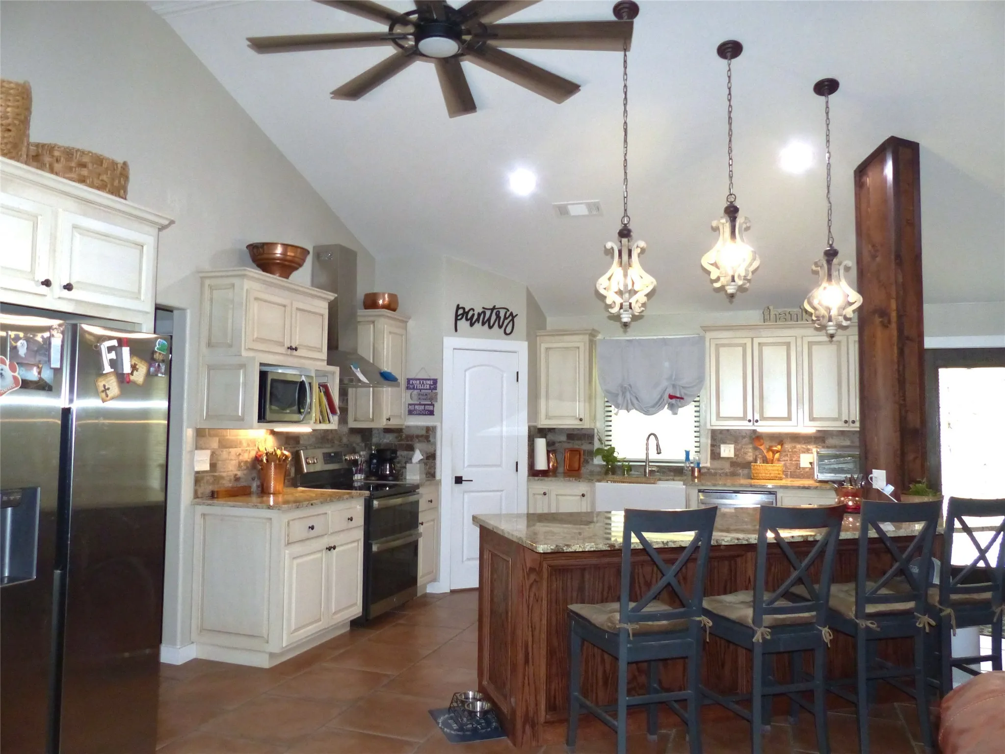 Kitchen featuring wall chimney range hood, tasteful backsplash, ceiling fan with notable chandelier, vaulted ceiling, and stainless steel appliances