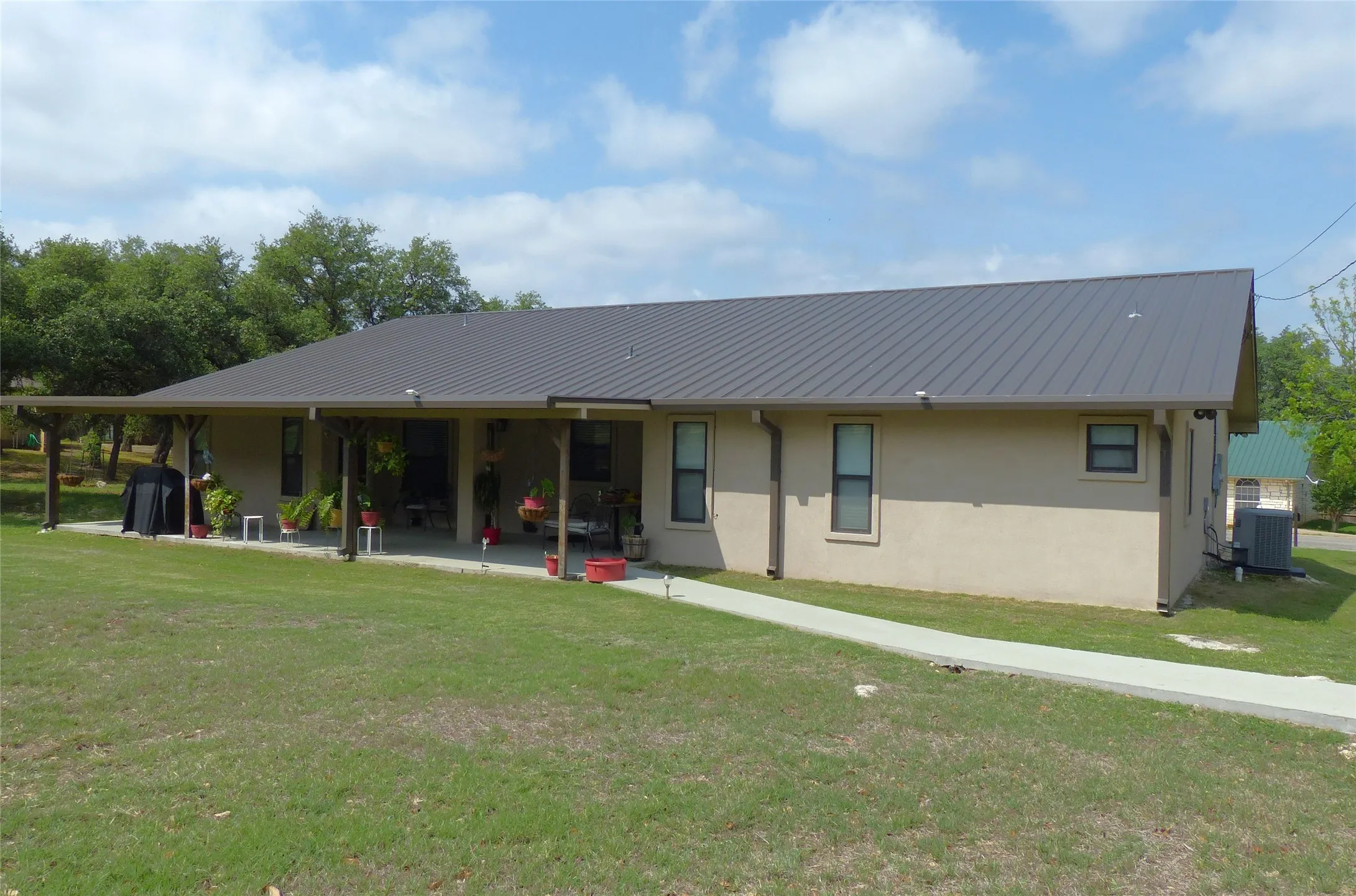 Rear view of house with stucco siding, central AC unit, a patio area, a yard, and metal roof