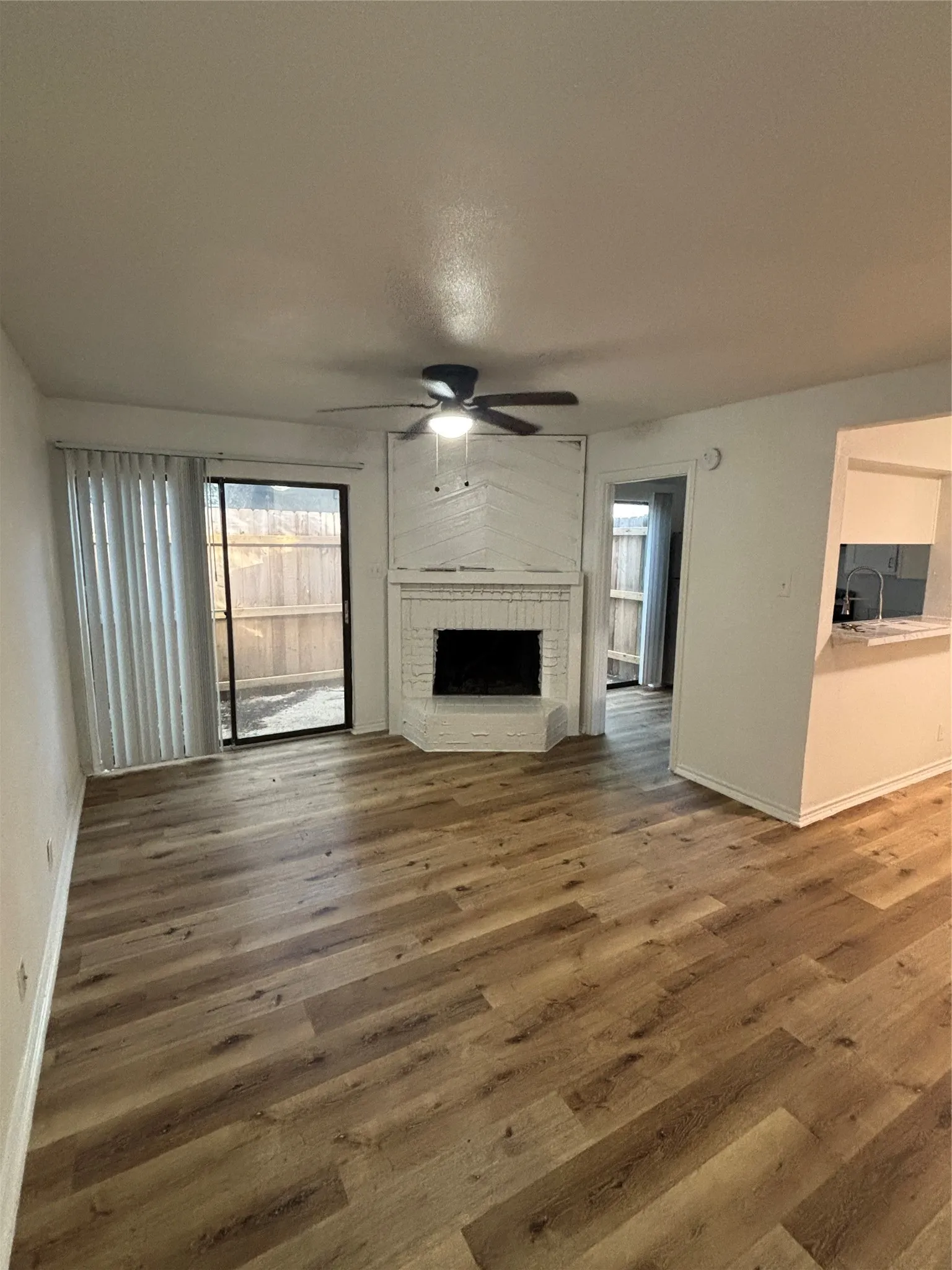 Spacious living area featuring wood-finish flooring, a corner fireplace with a white brick surround, and a ceiling fan