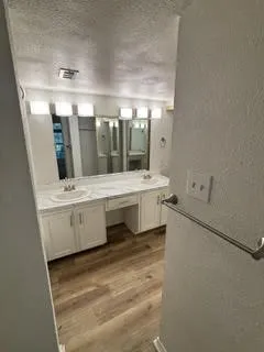 Dual vanity with undermount sinks and white cabinetry, a marble-patterned countertop, wood-finish flooring, and wall-mounted lighting fixtures