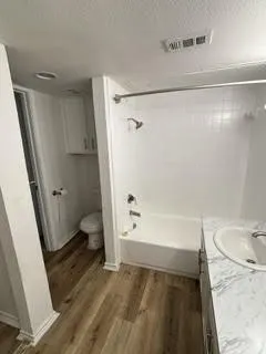Bathroom featuring wood-finish flooring, a white bathtub with subway tile surround, and a vanity with a white countertop and integrated sink