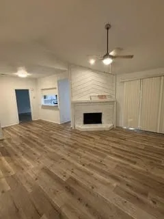 Spacious living area featuring wood-finish flooring, a white brick fireplace with a chevron-patterned overmantel, and a ceiling fan with integrated lighting