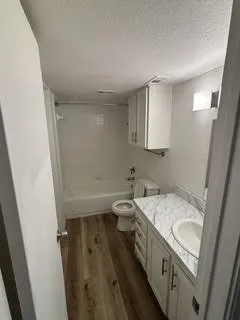 Bathroom featuring a white tub/shower combination, wood-finish flooring, a vanity with white cabinetry, a countertop with a marble-style finish, and a white integrated sink