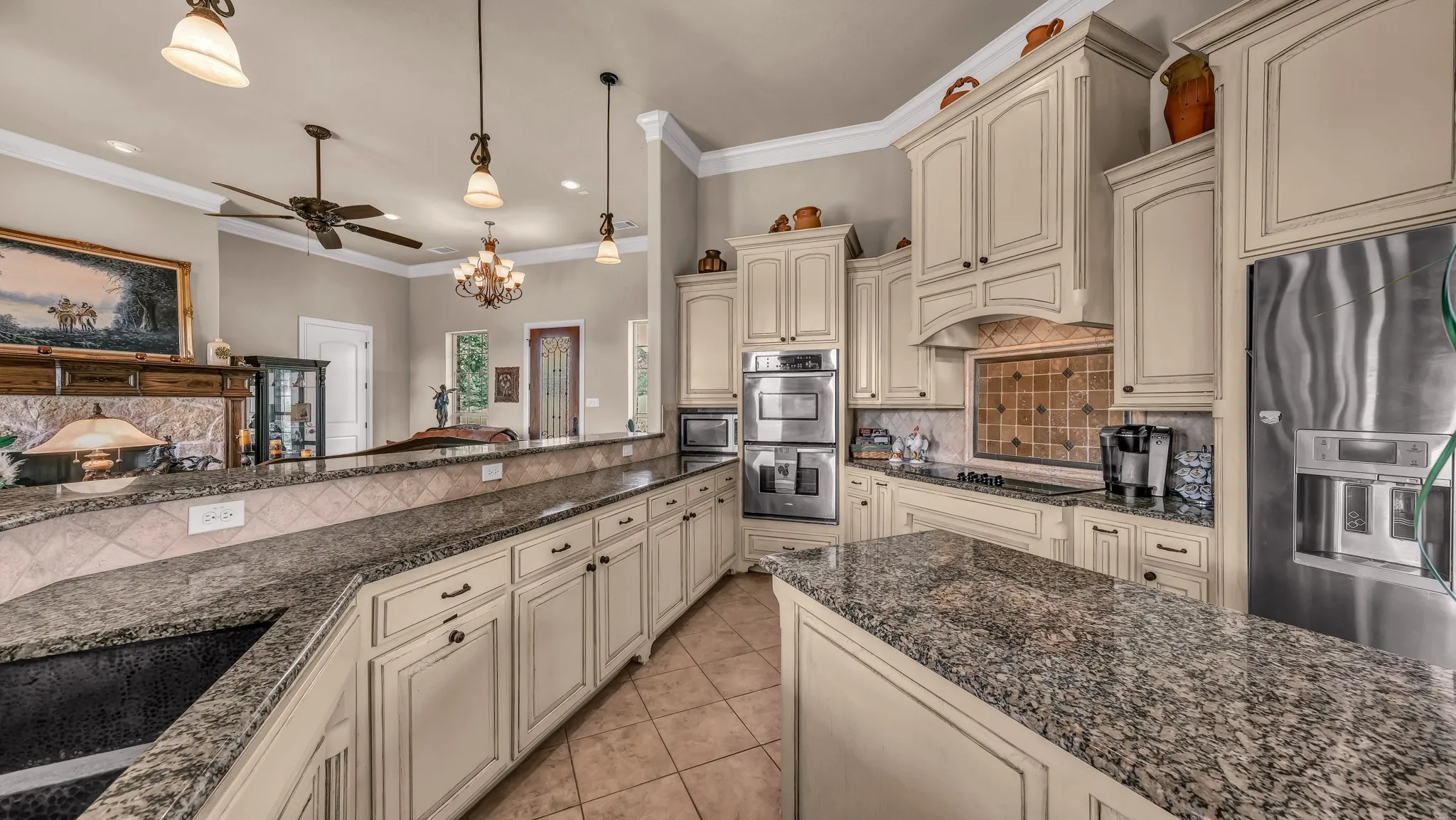 Kitchen with cream cabinets, crown molding, appliances with stainless steel finishes, ceiling fan with notable chandelier, and light tile patterned floors