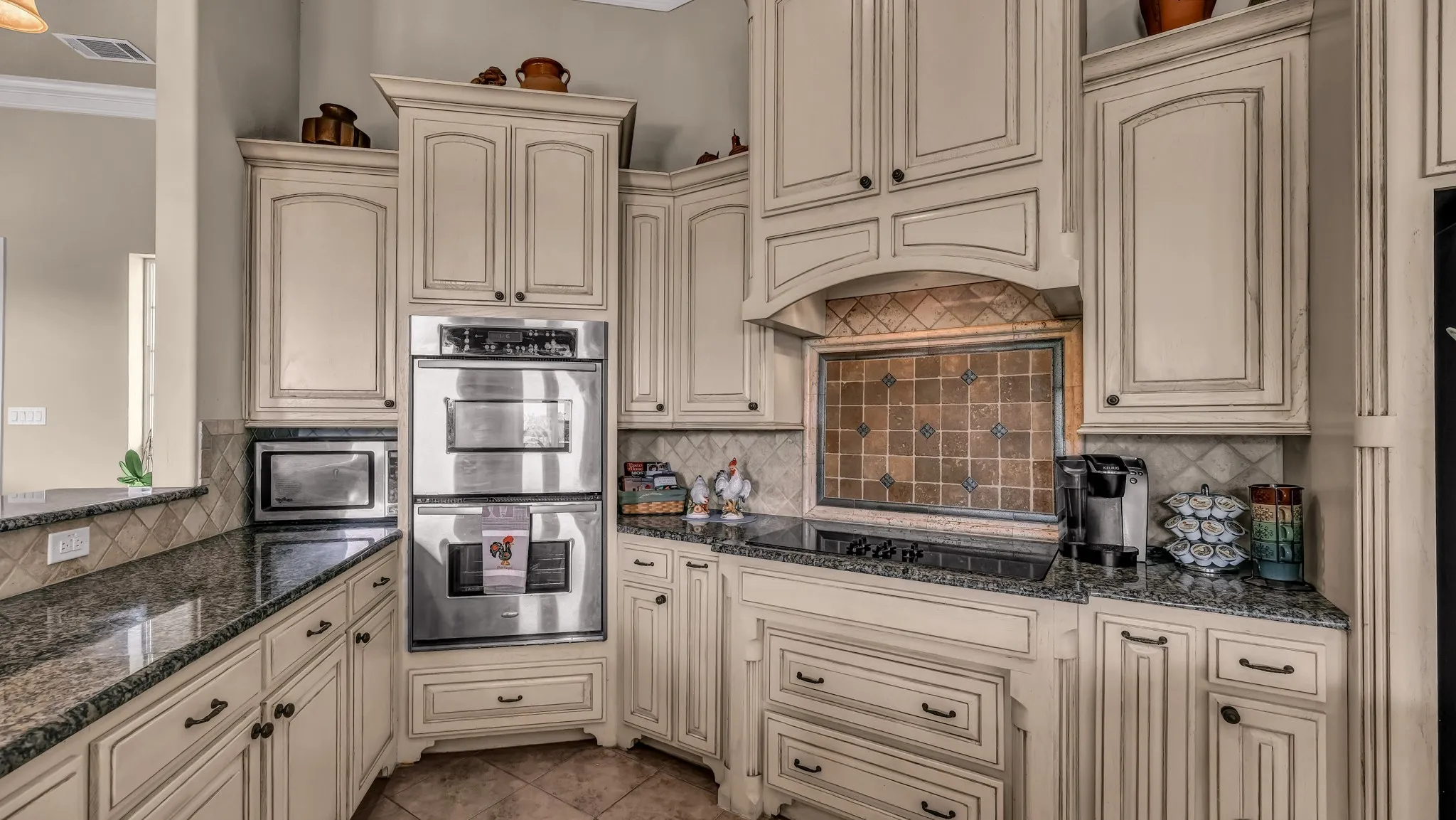 Kitchen with decorative backsplash, stainless steel double oven, black electric stovetop, and cream cabinetry