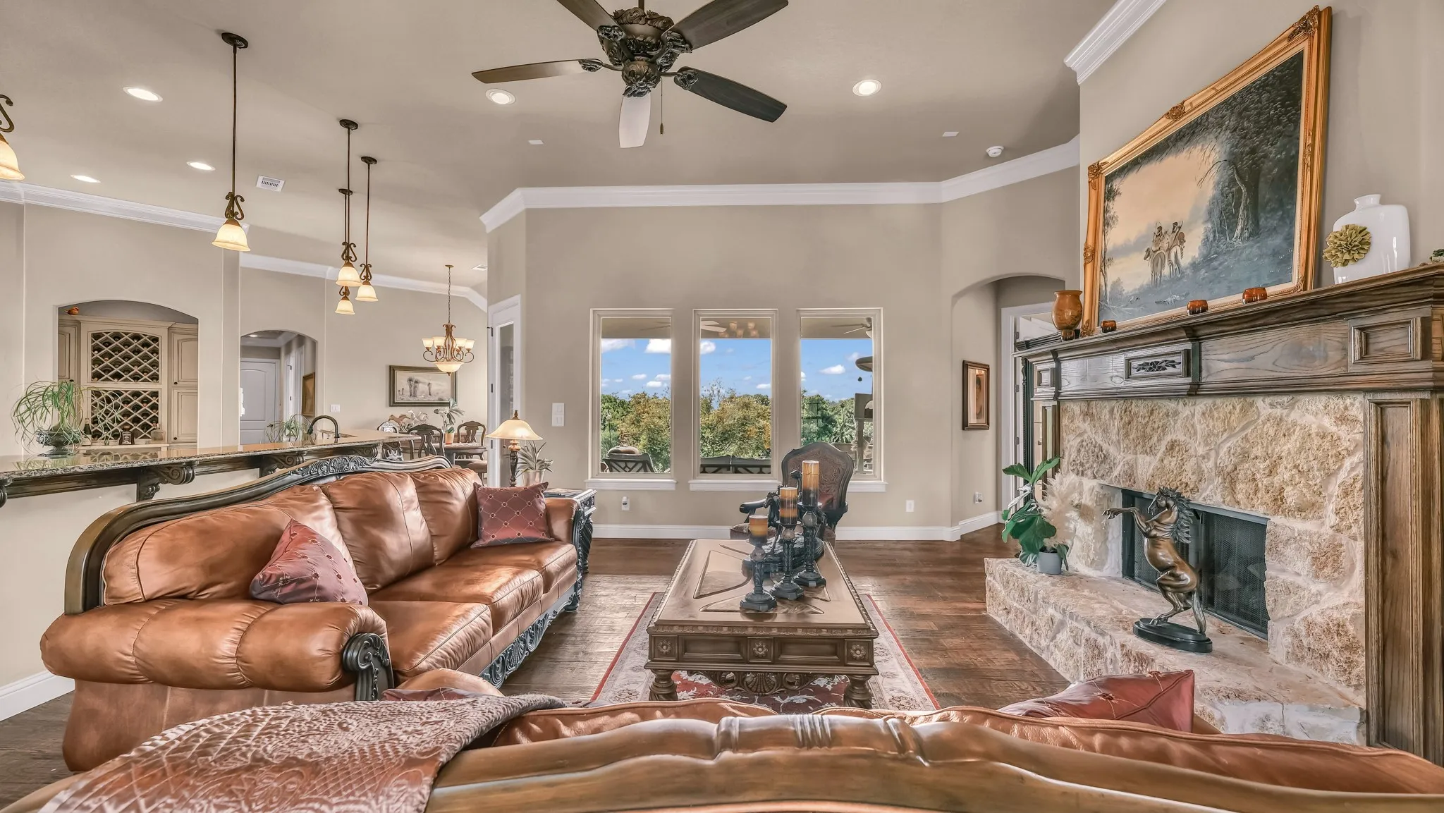 Living area with arched walkways, a stone fireplace, ceiling fan with notable chandelier, and dark wood-type flooring