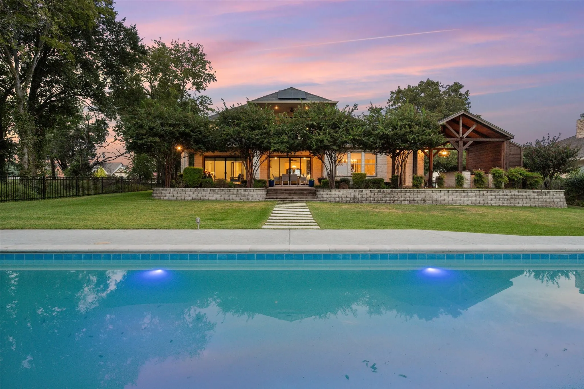 Welcome to 1140 The Shores Drive, where twilight transforms the backyard into a private resort with a shimmering pool, outdoor kitchen, and covered patios overlooking the lake.