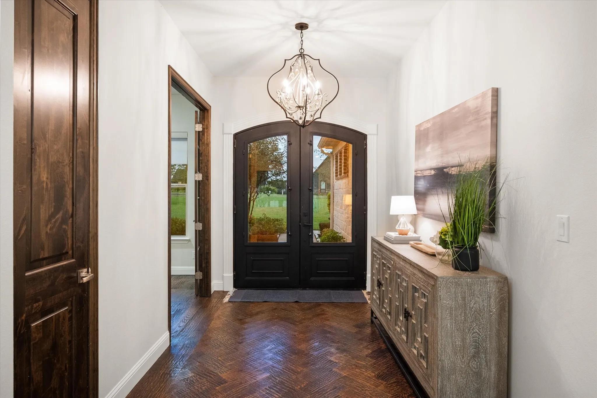 Sophisticated design elements, including herringbone floors, iron and glass doors, and statement lighting, define the entryway.