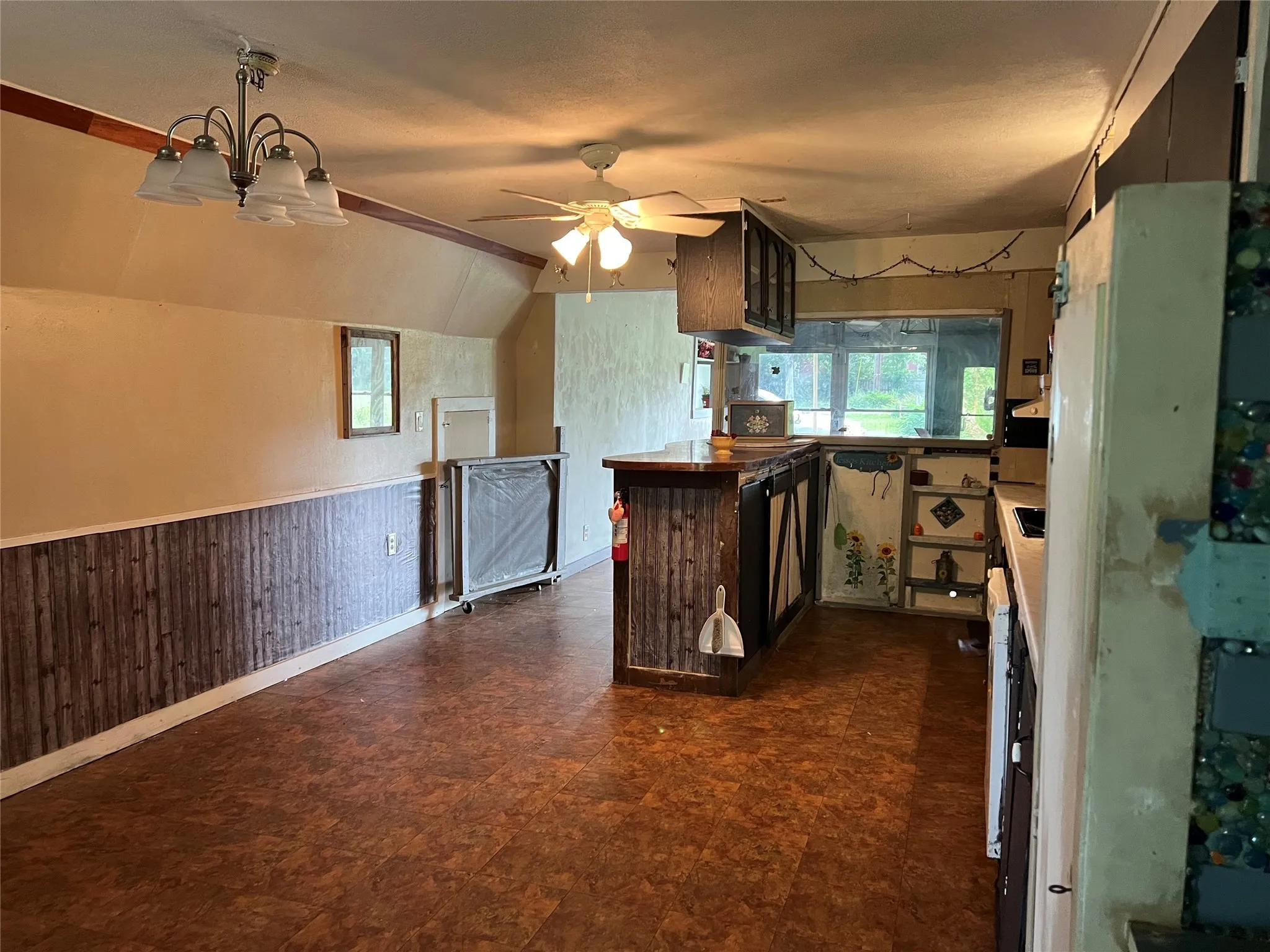 Kitchen with healthy amount of natural light, ceiling fan, dark floors, a wainscoted wall, and vaulted ceiling