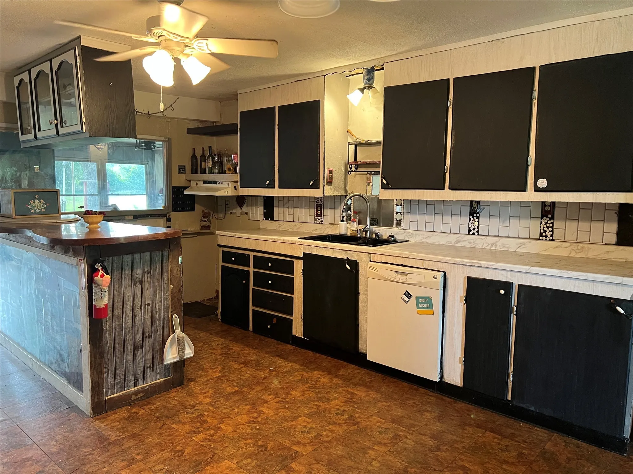 Kitchen featuring white dishwasher, dark cabinetry, tasteful backsplash, and a ceiling fan