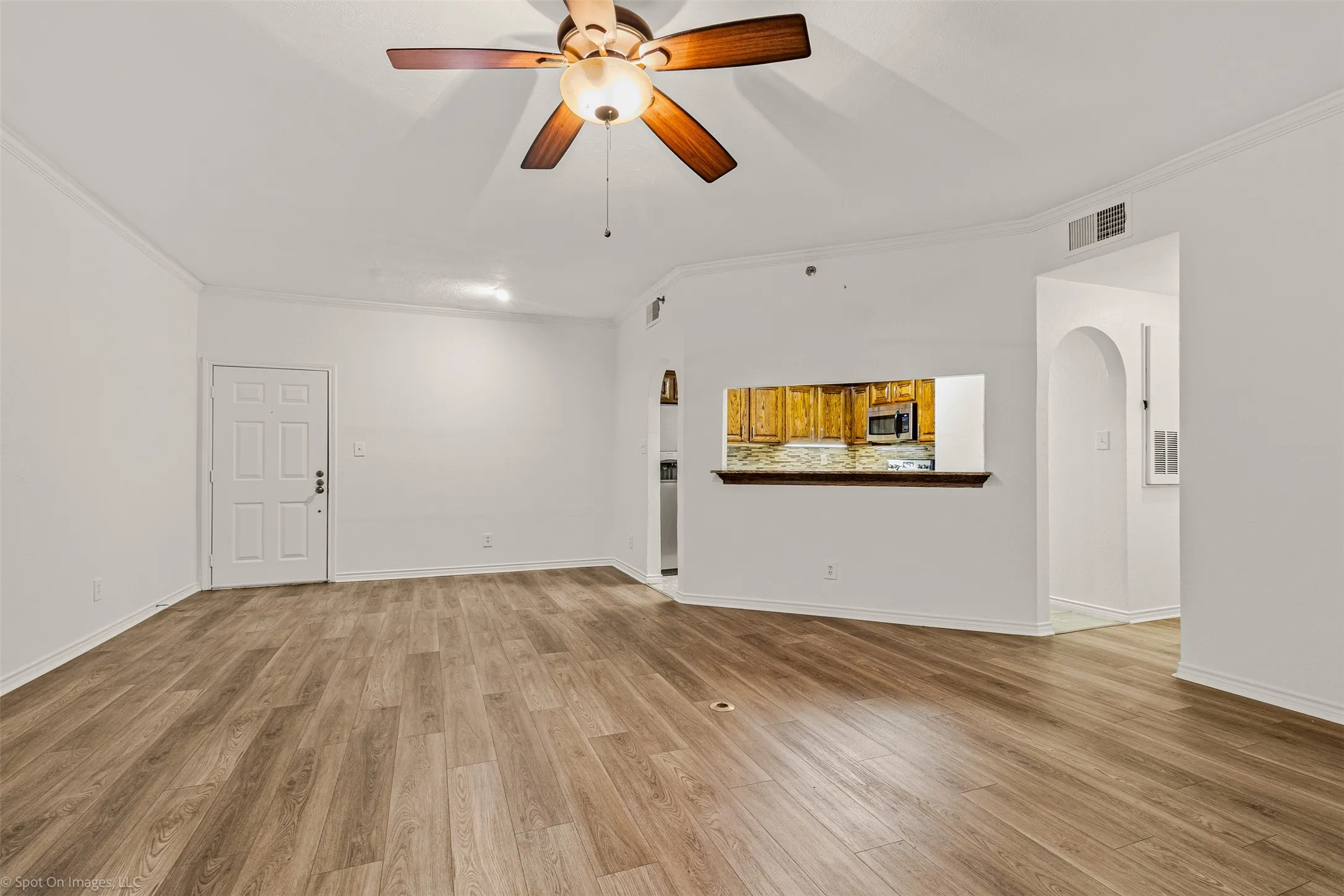 Unfurnished living room featuring light wood finished floors, crown molding, visible vents, and a ceiling fan