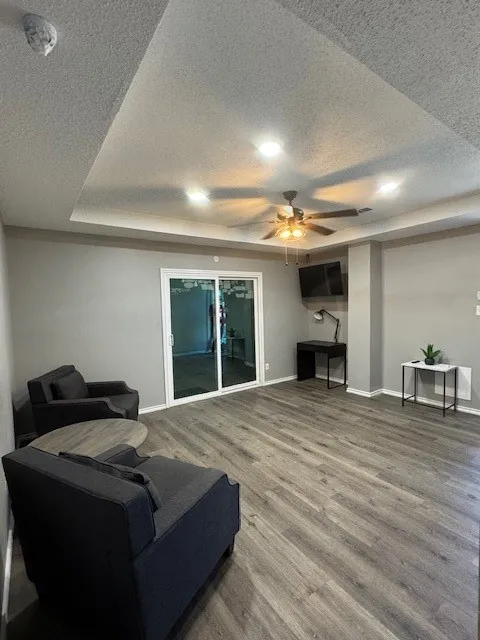 Living room featuring a textured ceiling, a ceiling fan, wood finished floors, and baseboards