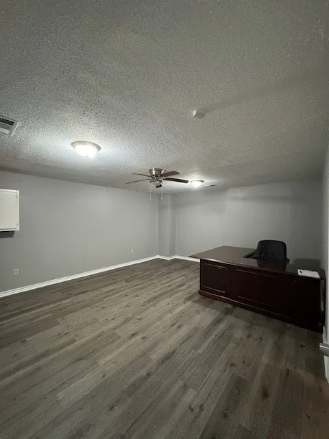 Basement featuring dark wood-style floors, a ceiling fan, a desk, baseboards, and a textured ceiling