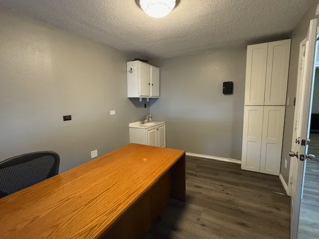 Office space featuring dark wood-style flooring, a textured ceiling, a sink, and baseboards