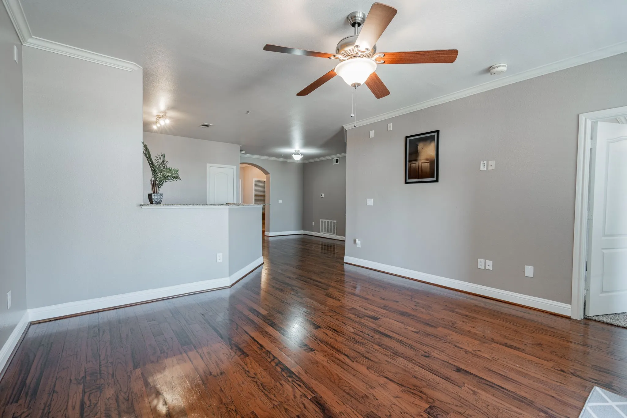 Unfurnished living room with arched walkways, ceiling fan, wood finished floors, baseboards, and crown molding