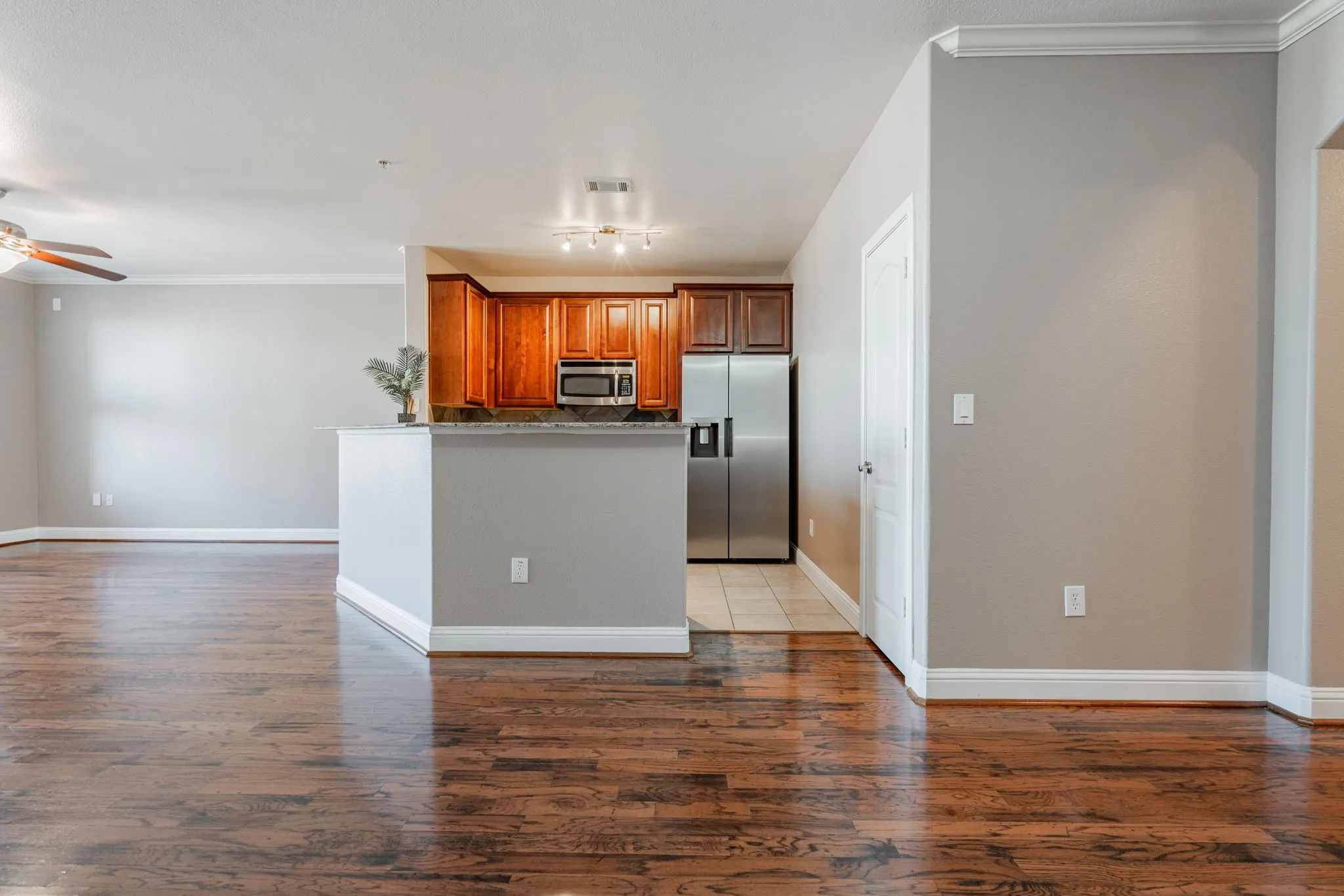 Kitchen featuring stainless steel appliances, a ceiling fan, crown molding, brown cabinets, and wood finished floors