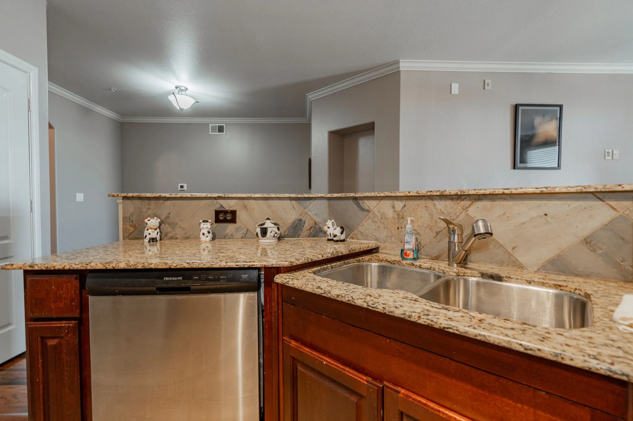 Kitchen with dishwasher, a sink, tasteful backsplash, ornamental molding, and light stone countertops