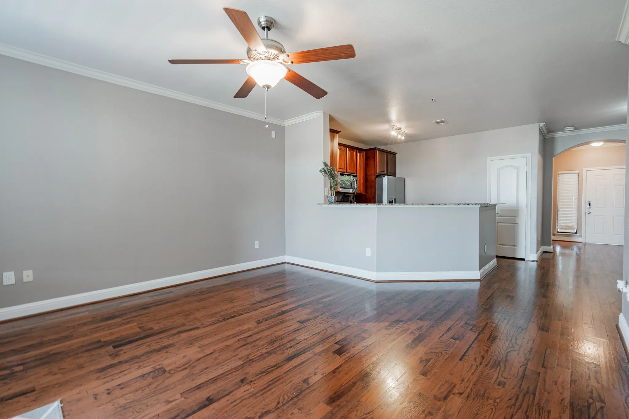 Unfurnished living room with arched walkways, a ceiling fan, dark wood-style floors, ornamental molding, and baseboards