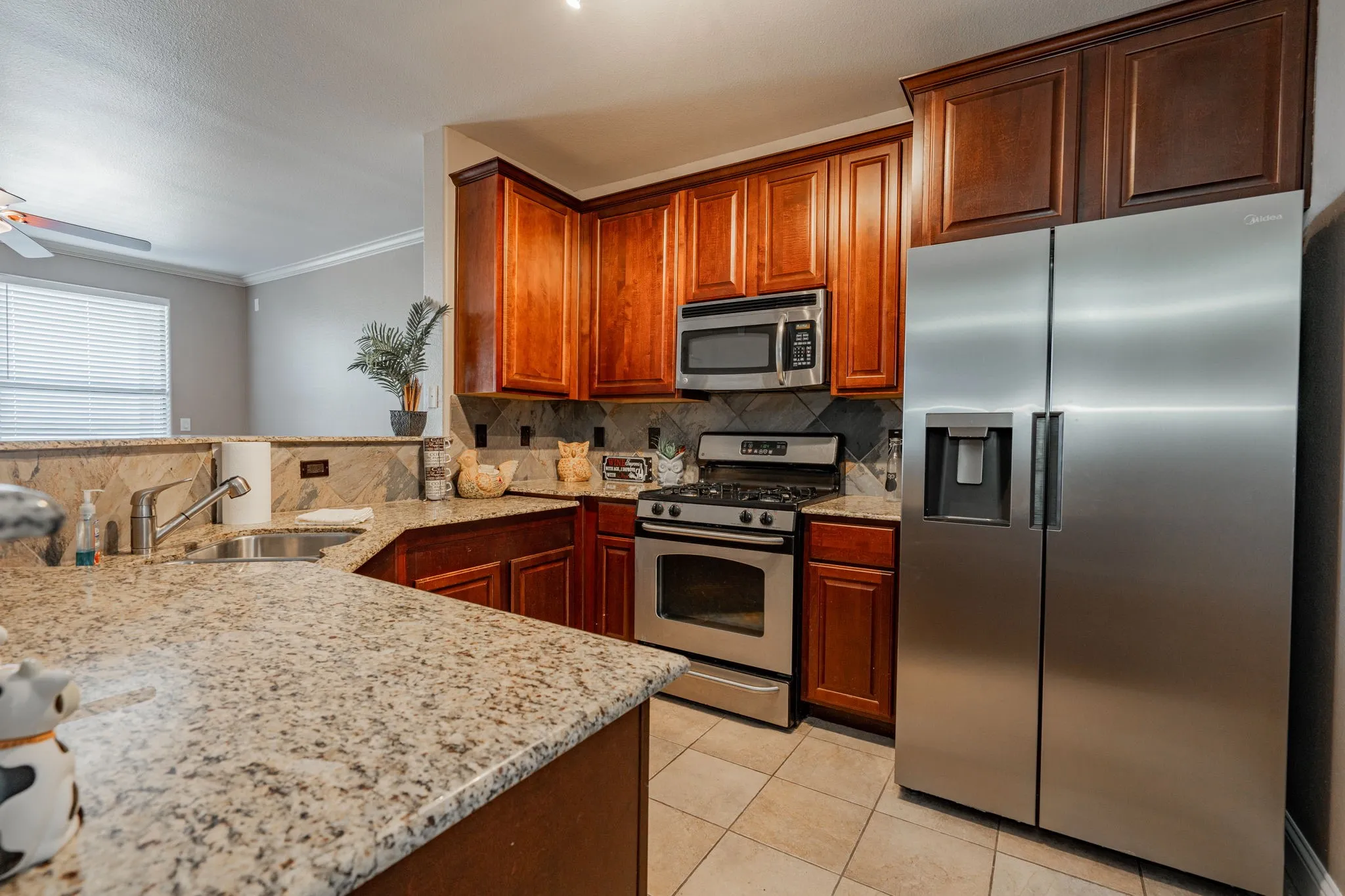 Kitchen featuring stainless steel appliances, backsplash, ornamental molding, a sink, and light tile patterned floors