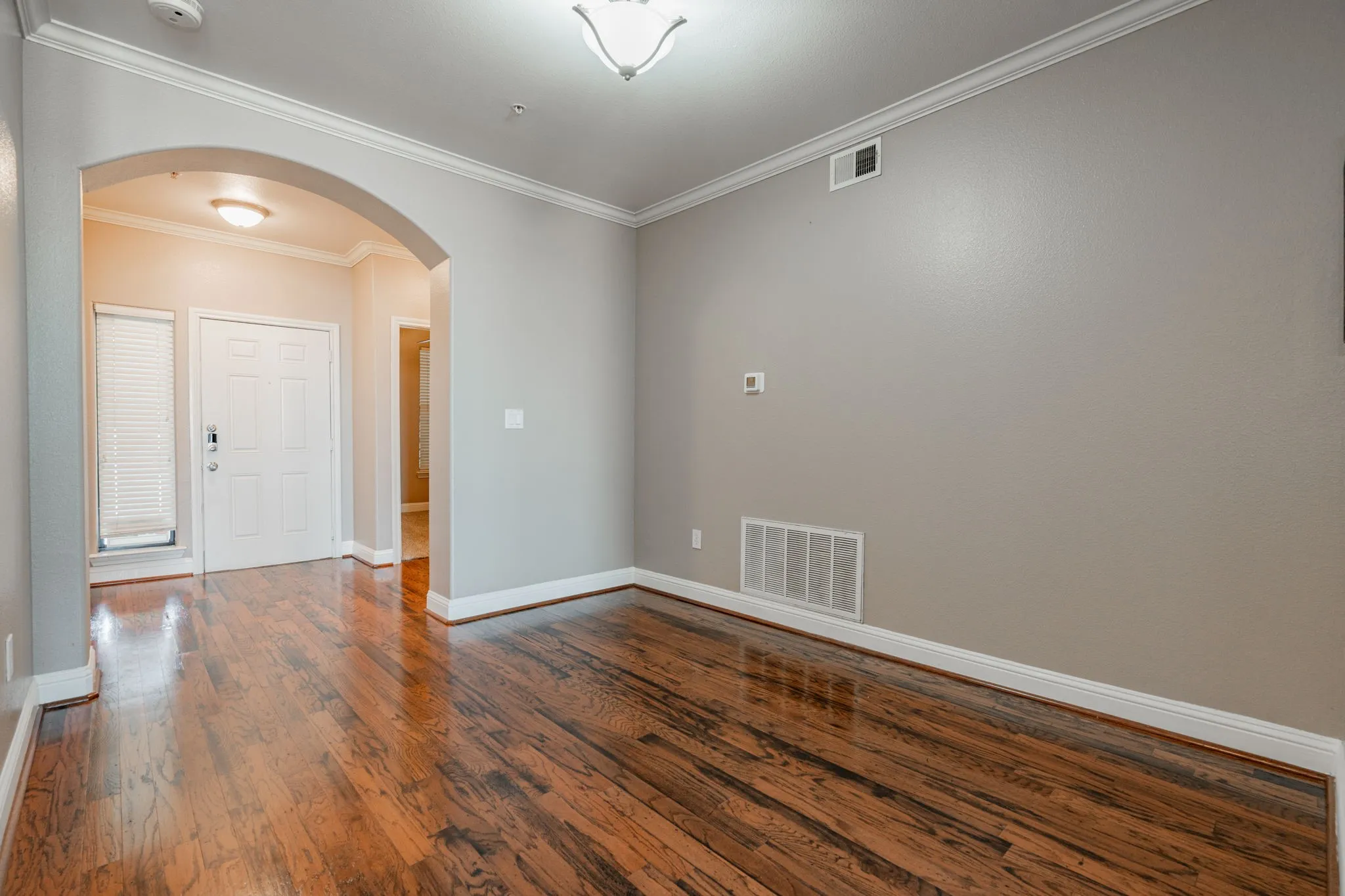 Spare room featuring arched walkways, dark wood-style floors, ornamental molding, and baseboards