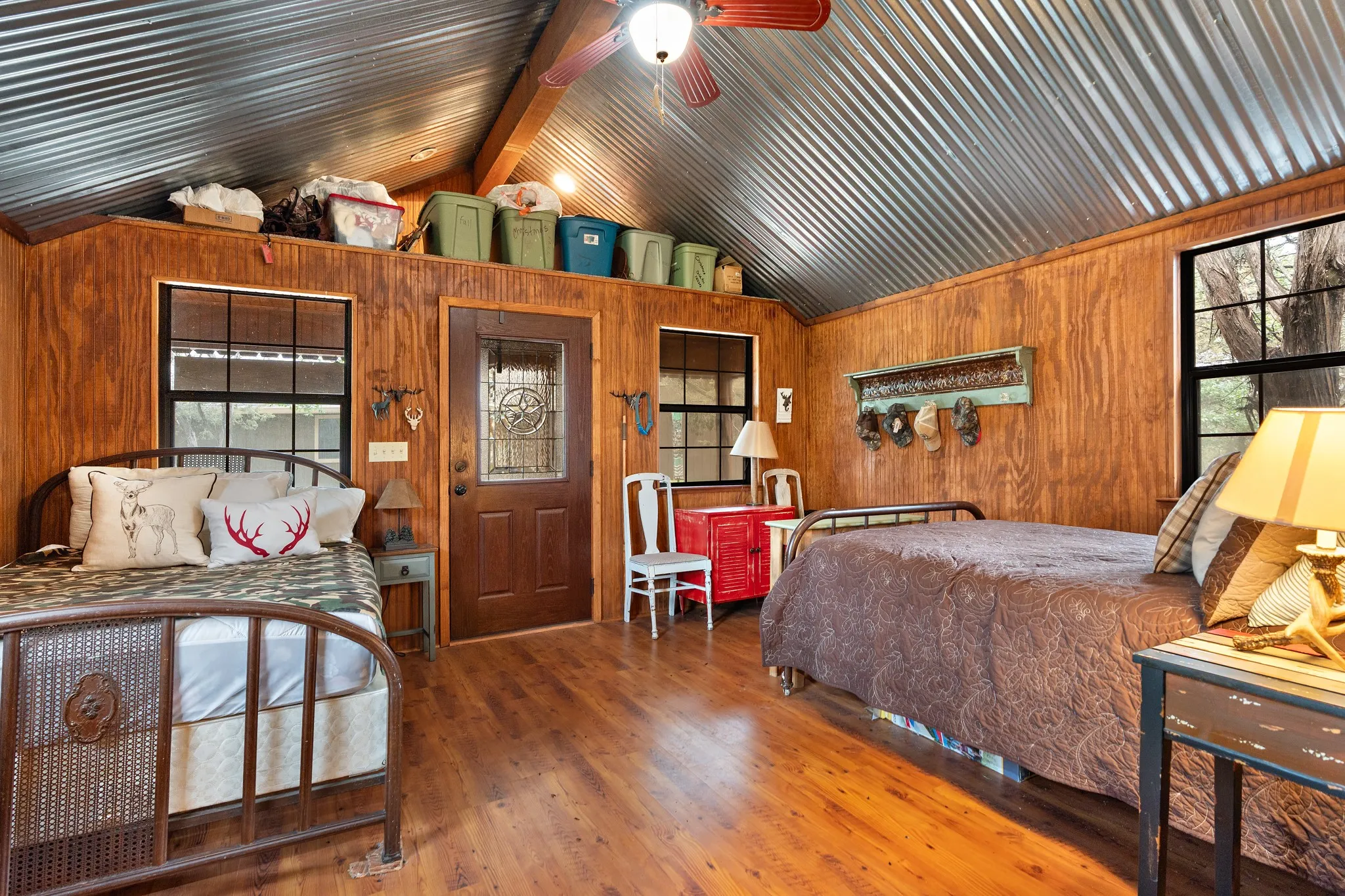 Bedroom with vaulted ceiling, multiple windows, wooden walls, and wood finished floors