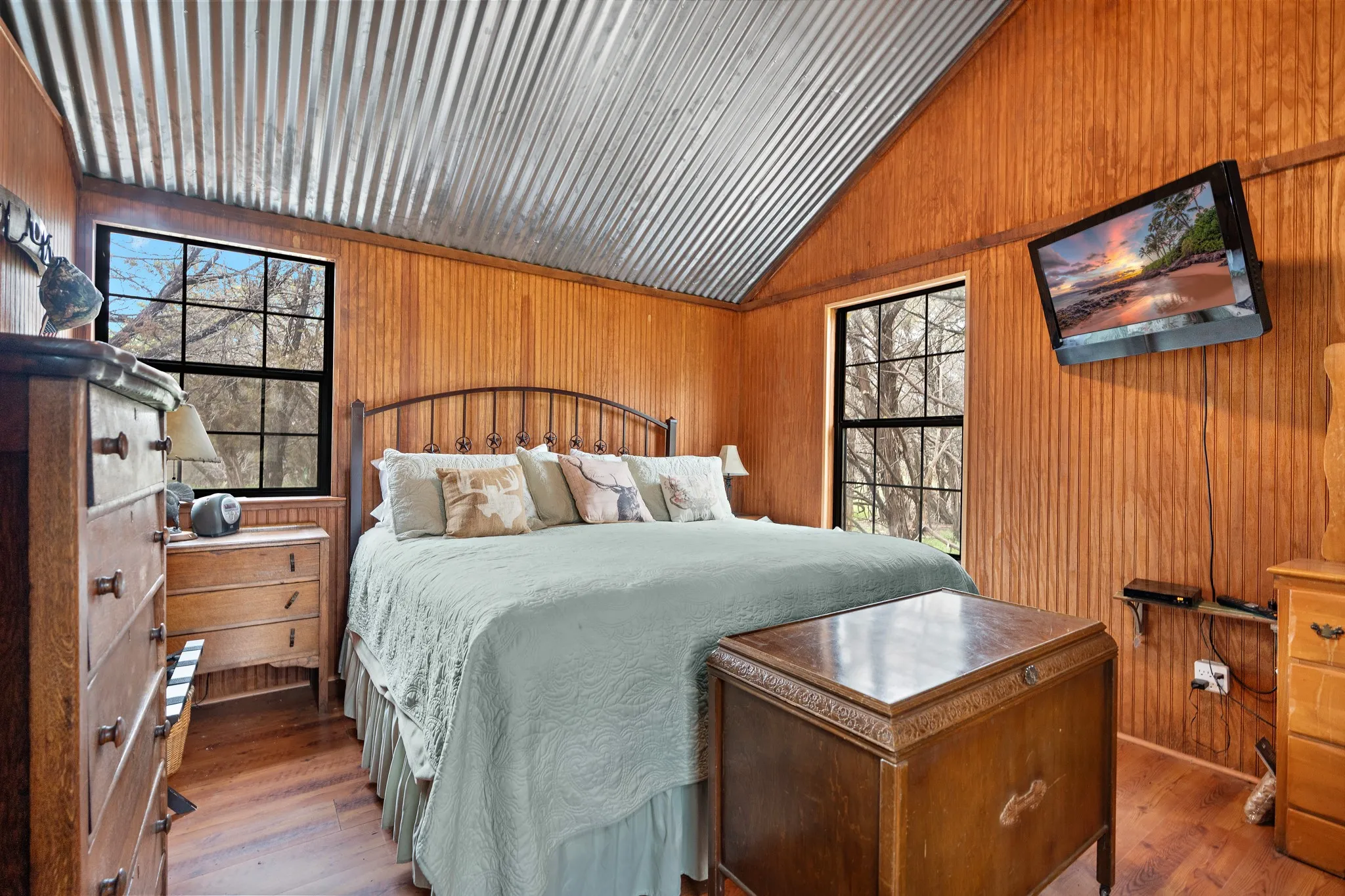 Bedroom with lofted ceiling, multiple windows, wooden walls, and wood finished floors