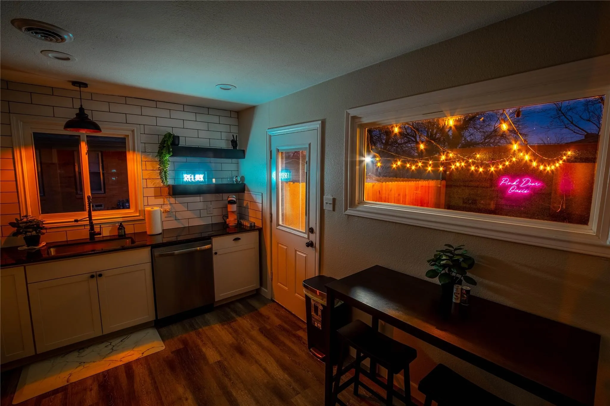 Kitchen with dishwasher, a sink, dark countertops, dark wood-style flooring, and decorative backsplash