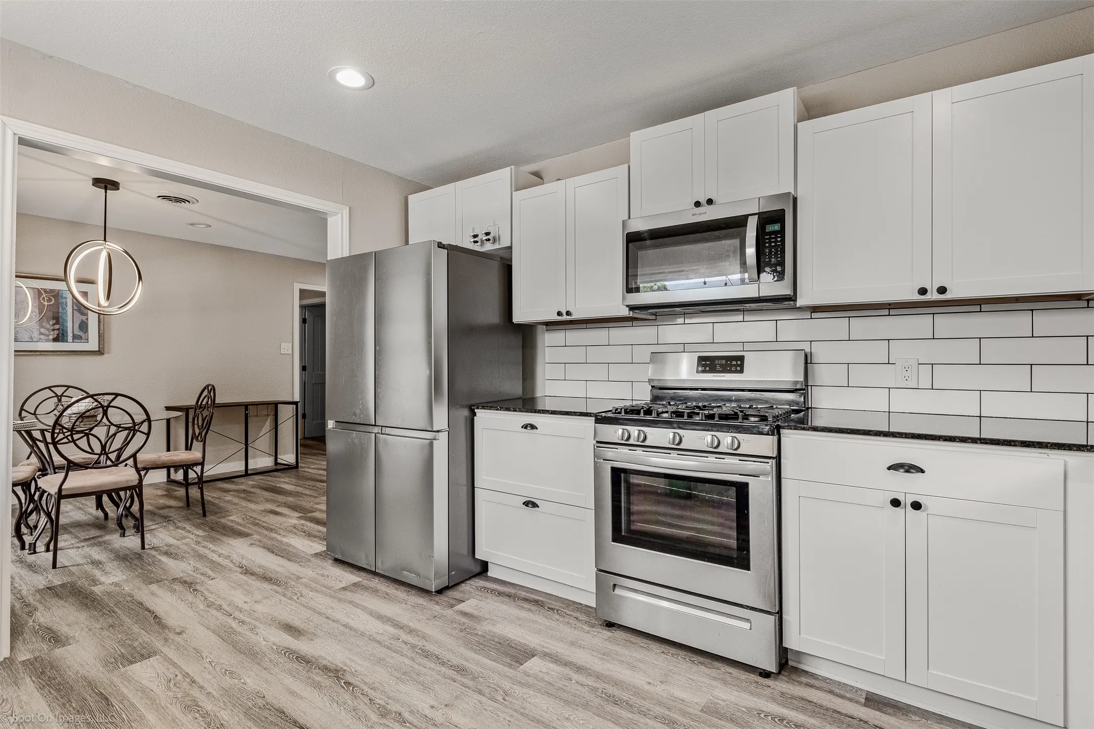 Kitchen with stainless steel appliances, light wood-type flooring, backsplash, white cabinets, and recessed lighting