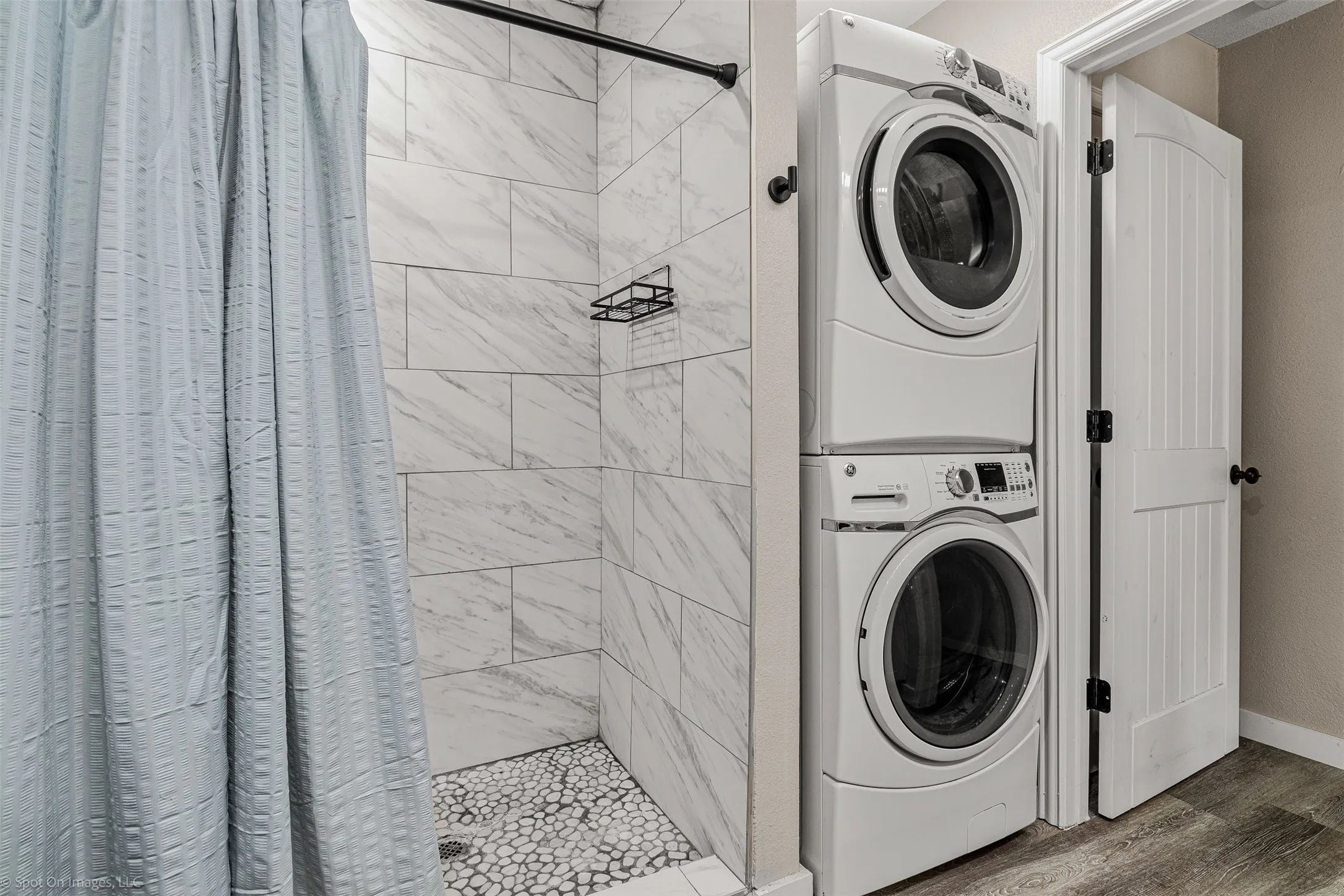 Washroom featuring stacked washing machine and dryer, wood finished floors, and baseboards